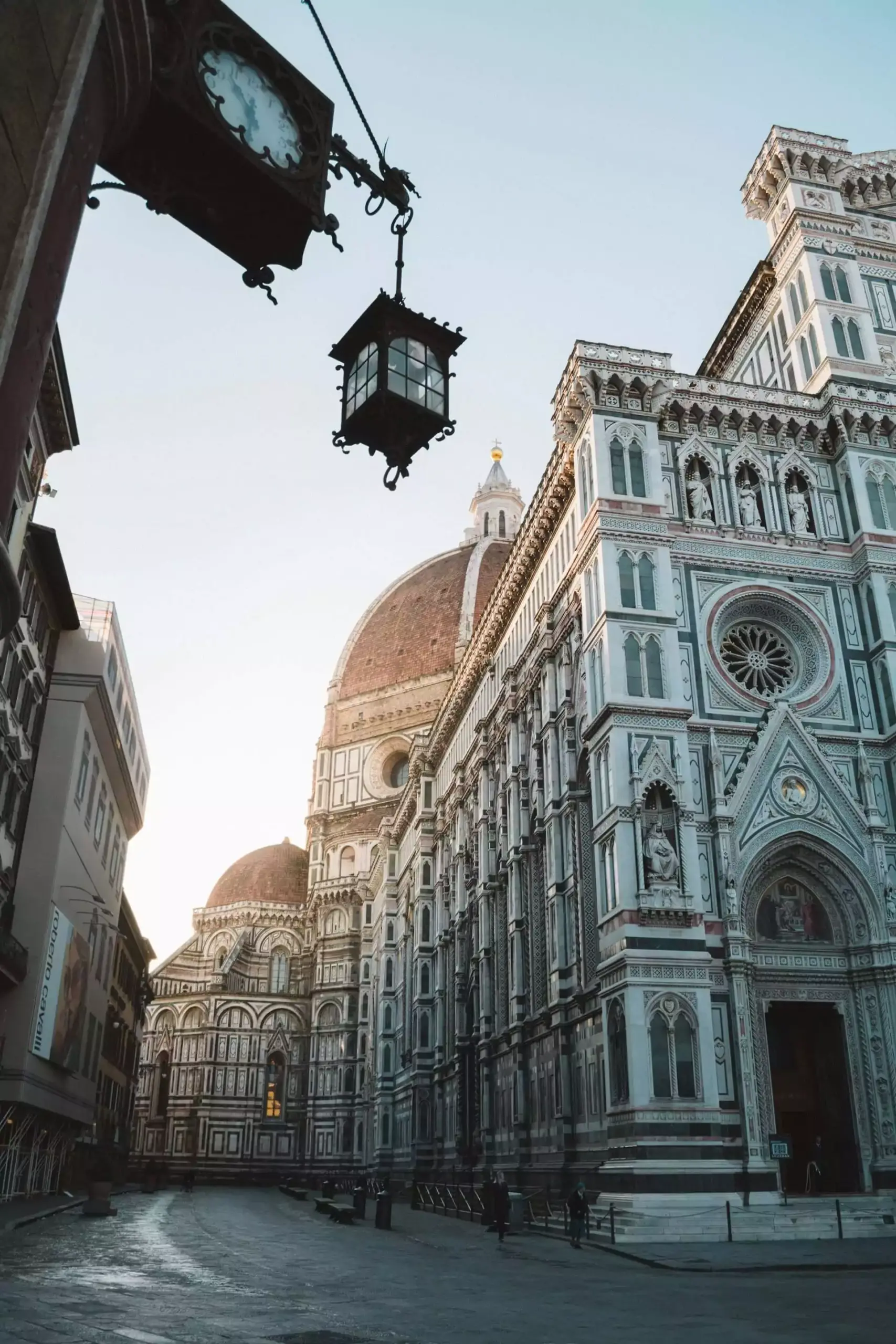 Florence’s Duomo, or Cathedral of Santa Maria del Fiore, glowing in the golden light of sunset, with its red-tiled dome and marble façade standing out against the colorful evening sky.