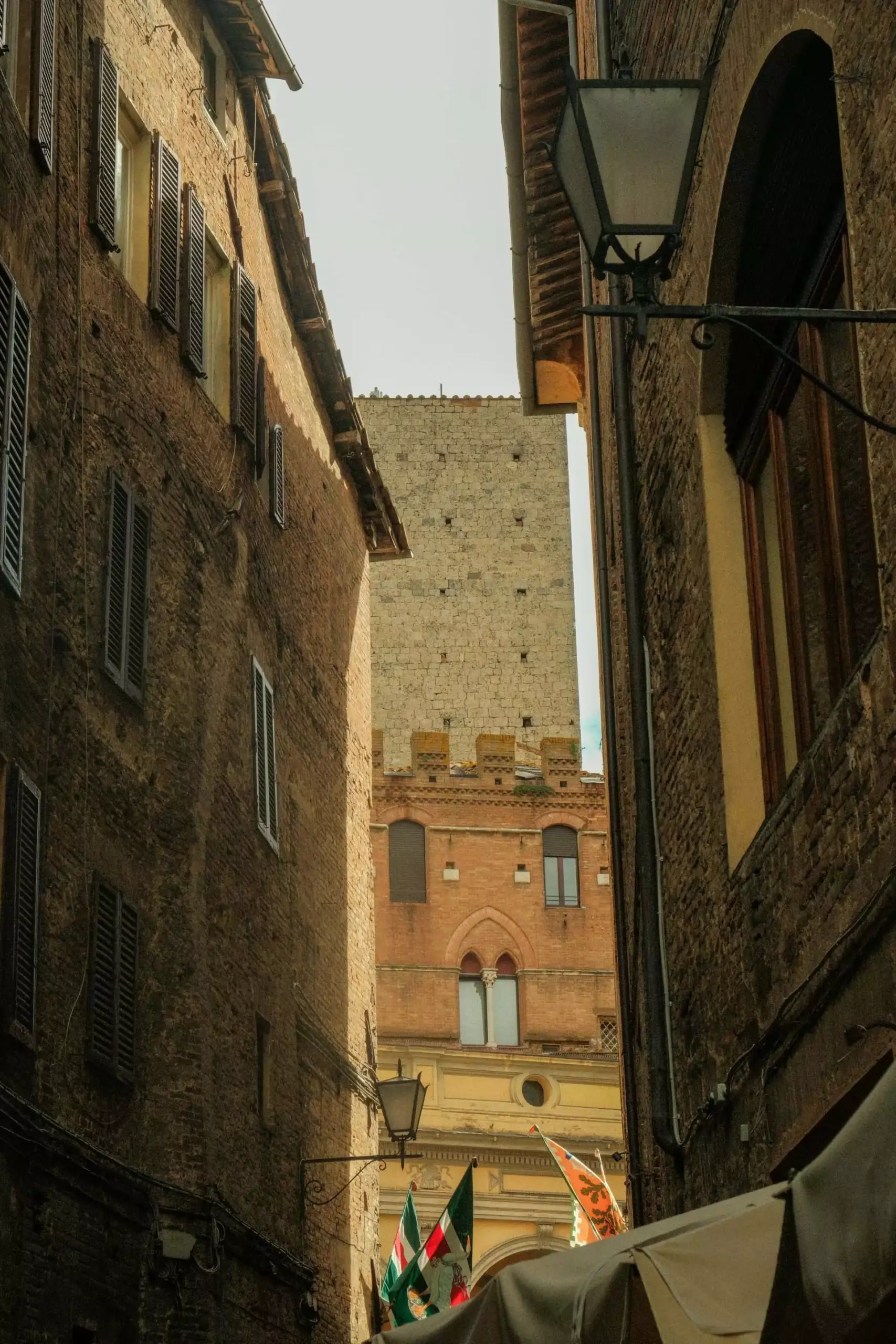 Piazza in San Gimignano, Italy, surrounded by medieval stone buildings and towers, with cafés, shops, and visitors gathered around the cobblestone square in the heart of the historic hilltop town.