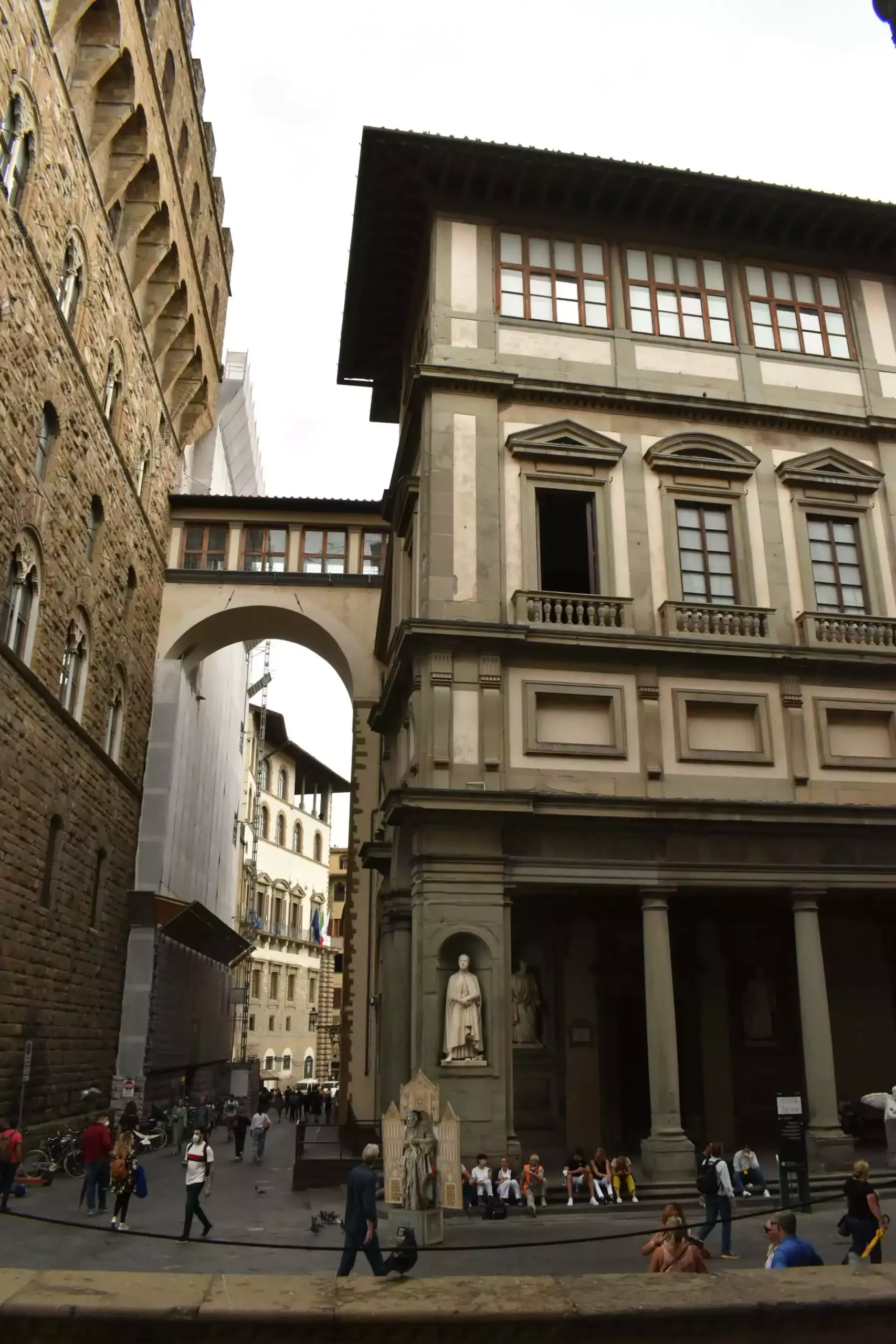 Exterior of the Uffizi Galleries in Florence, Italy, featuring long symmetrical colonnades, arched windows, and Renaissance architectural details leading to the scenic view of the Arno River.
