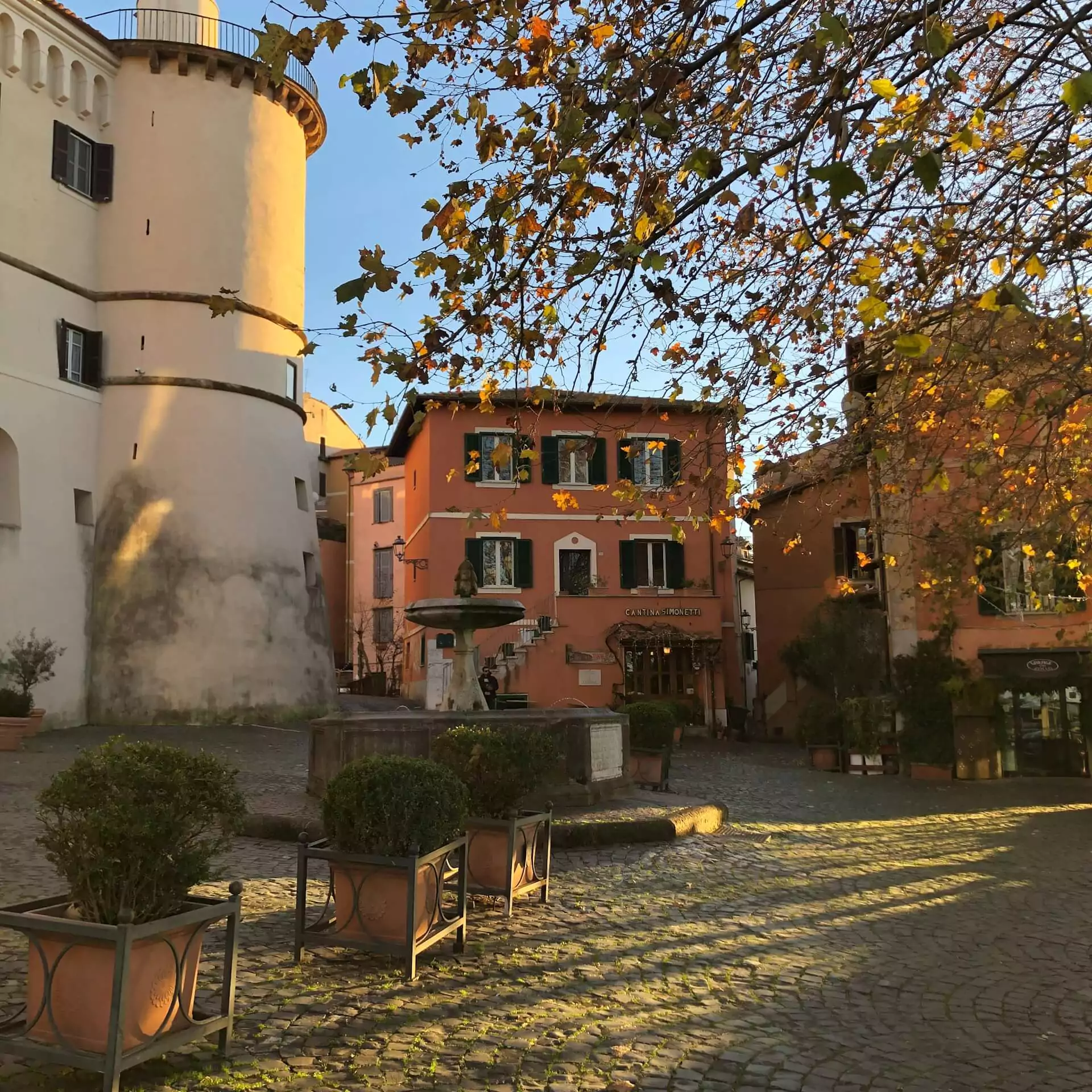 Building with a clock tower in the center of a courtyard at Piazza San Rocco in Frascati, Italy, featuring arched windows, warm-toned walls, and a central open space surrounded by historic architecture.