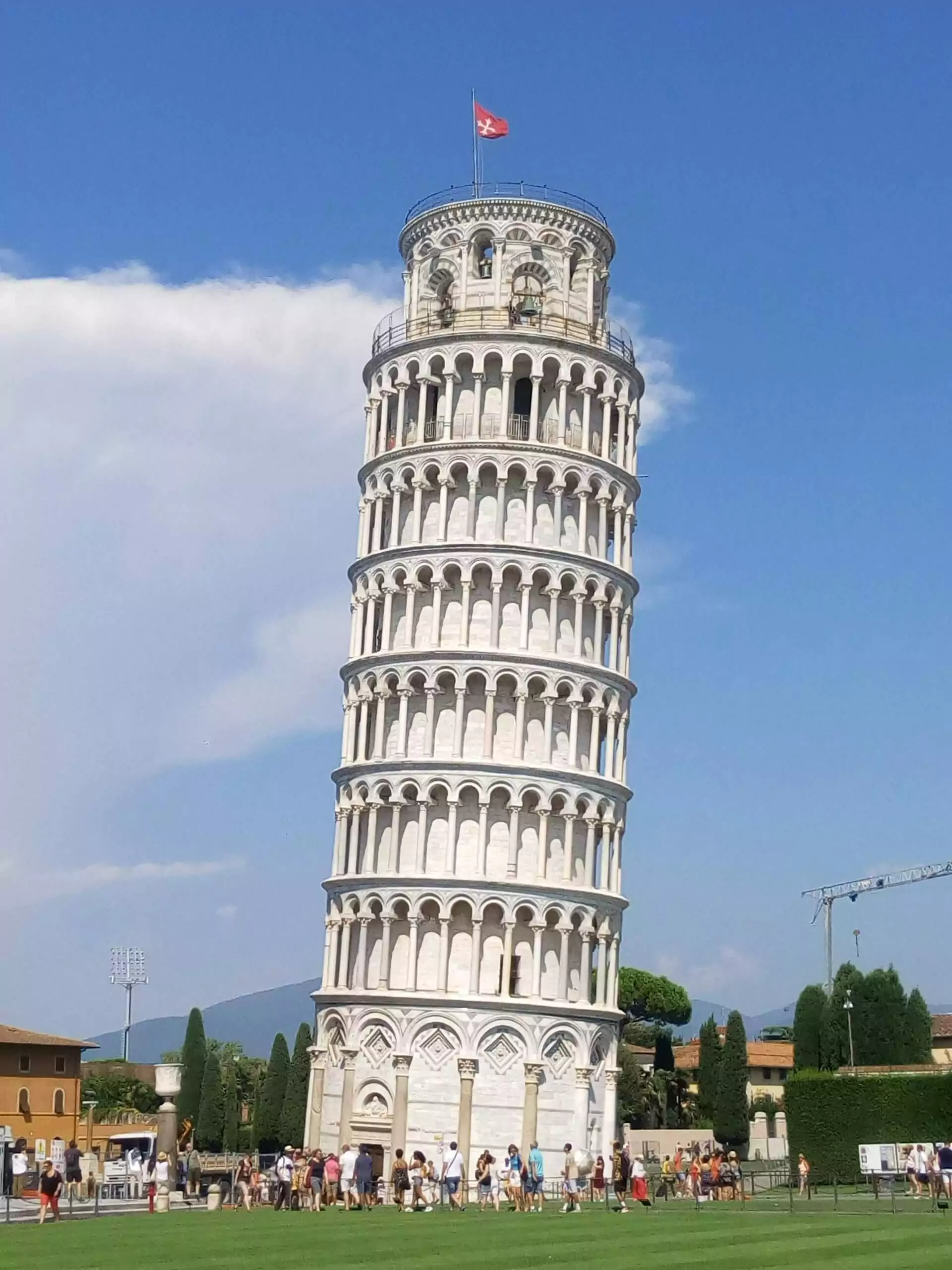 The Leaning Tower of Pisa in Italy, with its distinct tilt and white marble Romanesque architecture, standing next to the Pisa Cathedral on the grassy Piazza dei Miracoli under a bright sky.