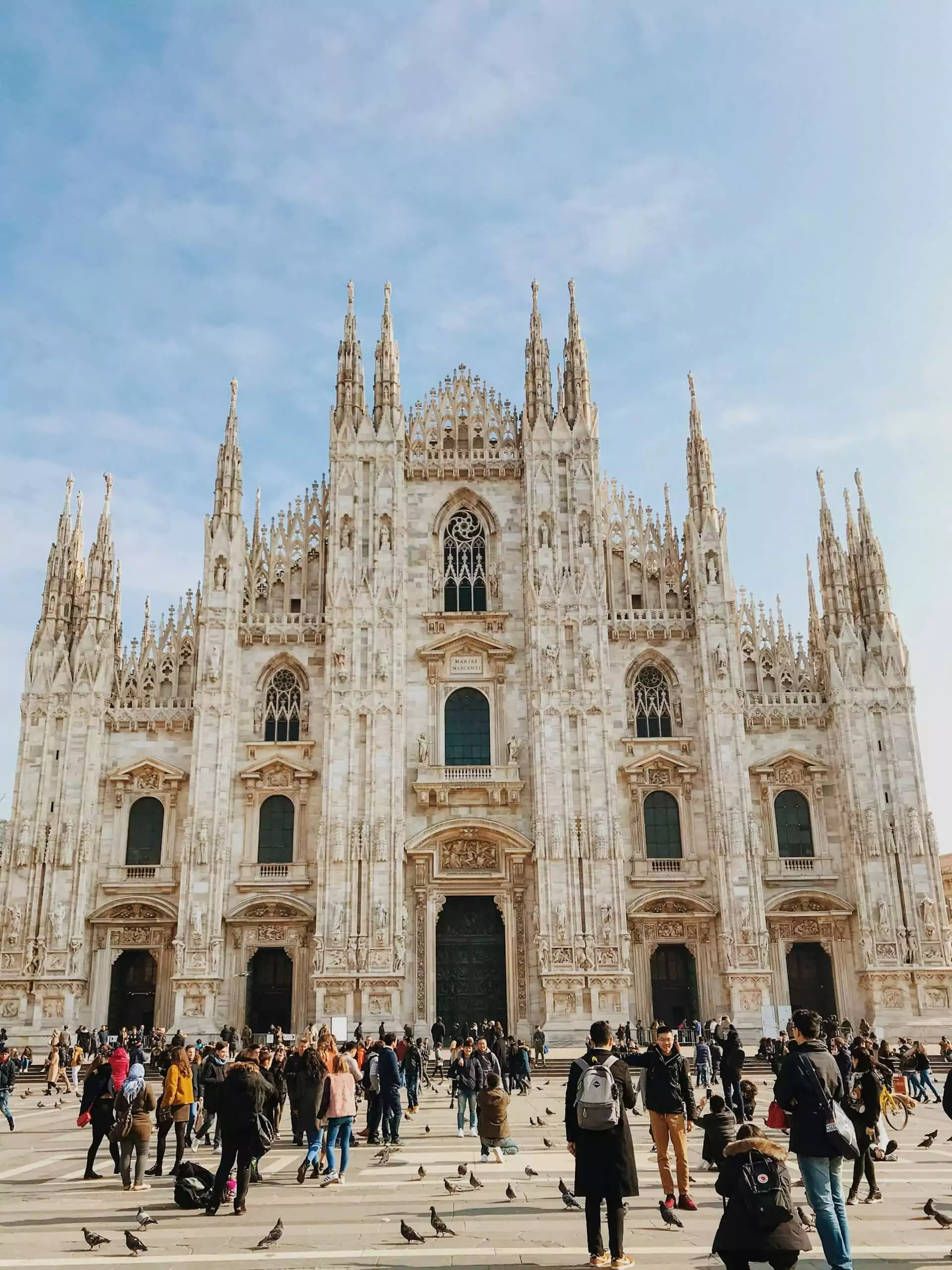Milan Cathedral (Duomo di Milano) in Italy, featuring its elaborate Gothic façade with countless spires, statues, and ornate carvings, standing prominently in the city’s central square under a bright sky.