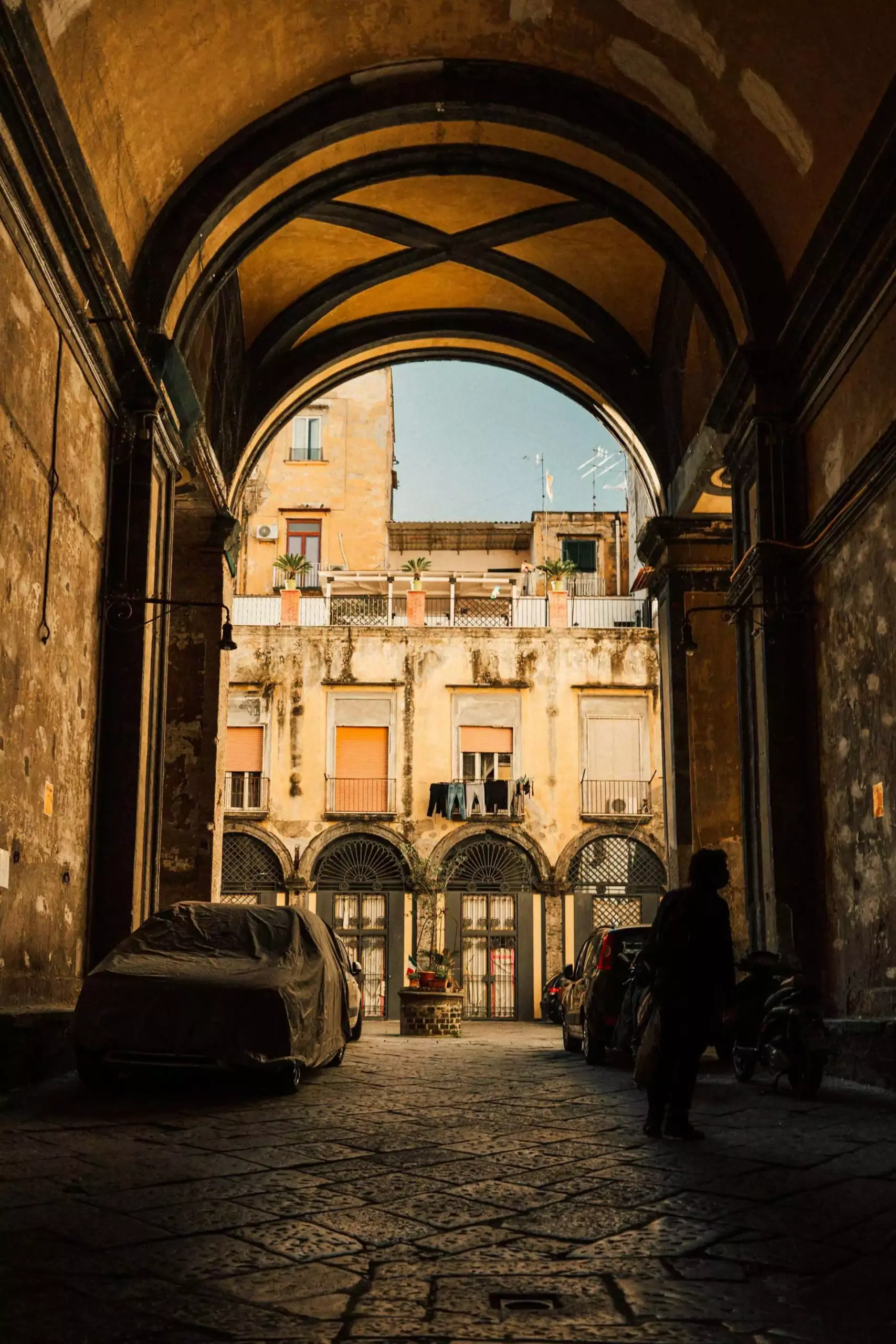 Stone arch passage in the historic streets of Naples, Italy, connecting aged buildings with rustic balconies and adding character to the narrow, shadowed alleyway.