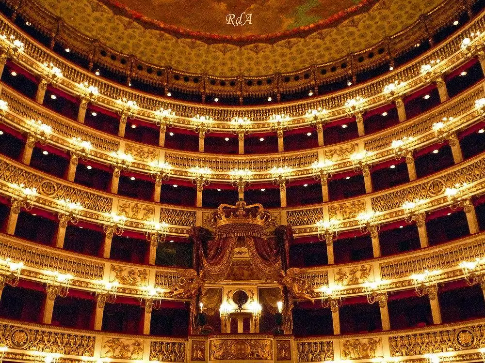 Interior of the San Carlo Theatre in Naples, Italy, featuring ornate gold balconies, red velvet seats, and a grand chandelier hanging from a frescoed ceiling, reflecting the opulence of one of Europe’s oldest opera houses.