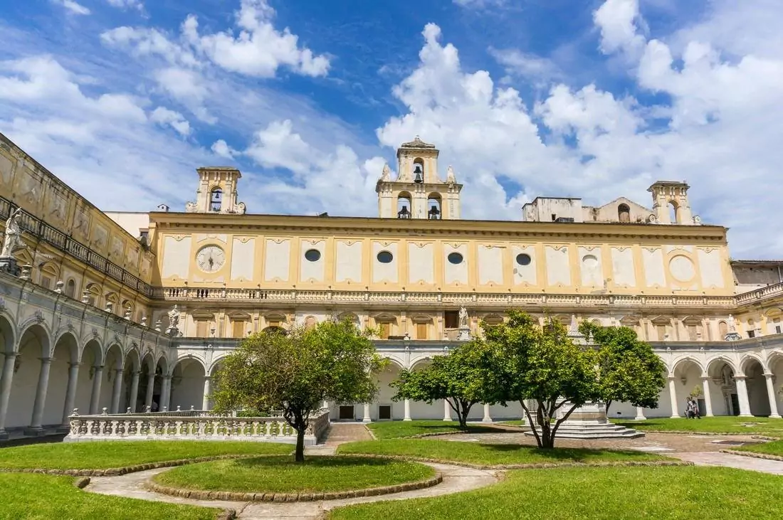 Exterior of Certosa e Museo di San Martino in Naples, Italy, featuring grand white Baroque architecture perched on a hill, with sweeping views of the city and the Bay of Naples below.