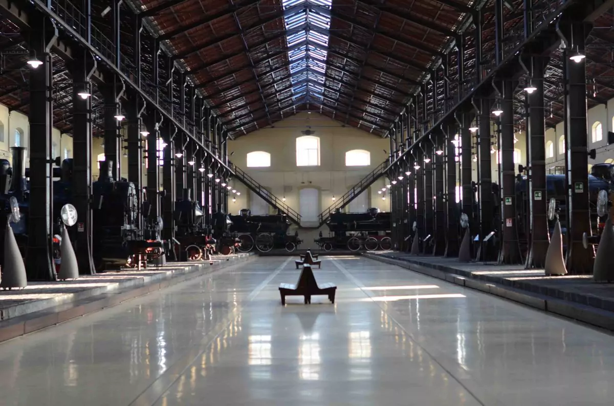 Interior of the Museo Nazionale Ferroviario di Pietrarsa in Naples, Italy, showcasing historic locomotives and railway cars inside a large former industrial complex with high arched ceilings and iron beams.