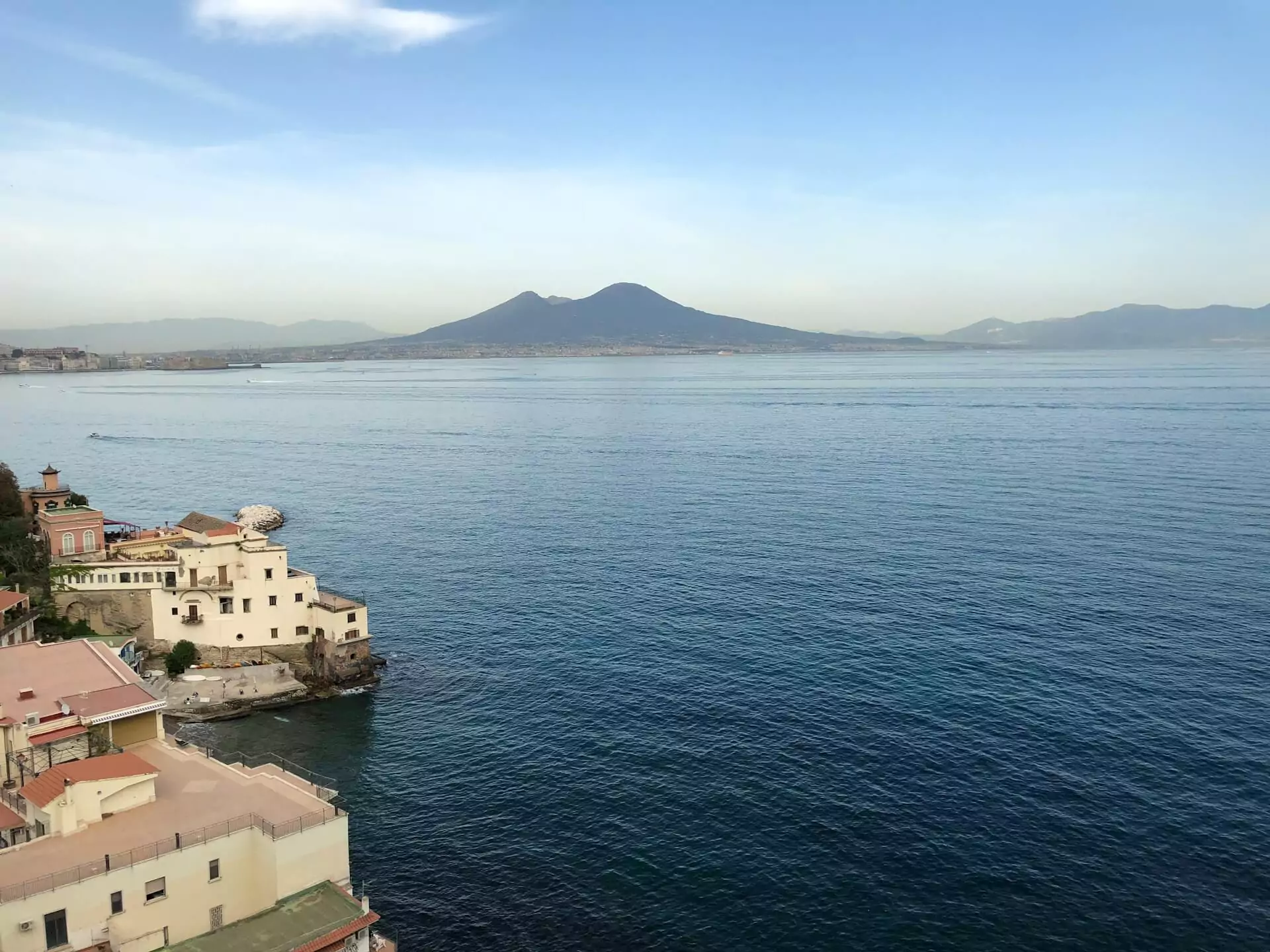 Posillipo neighborhood in Naples, Italy, with hillside villas overlooking the Bay of Naples, lush greenery, and a clear view of Mount Vesuvius in the distance