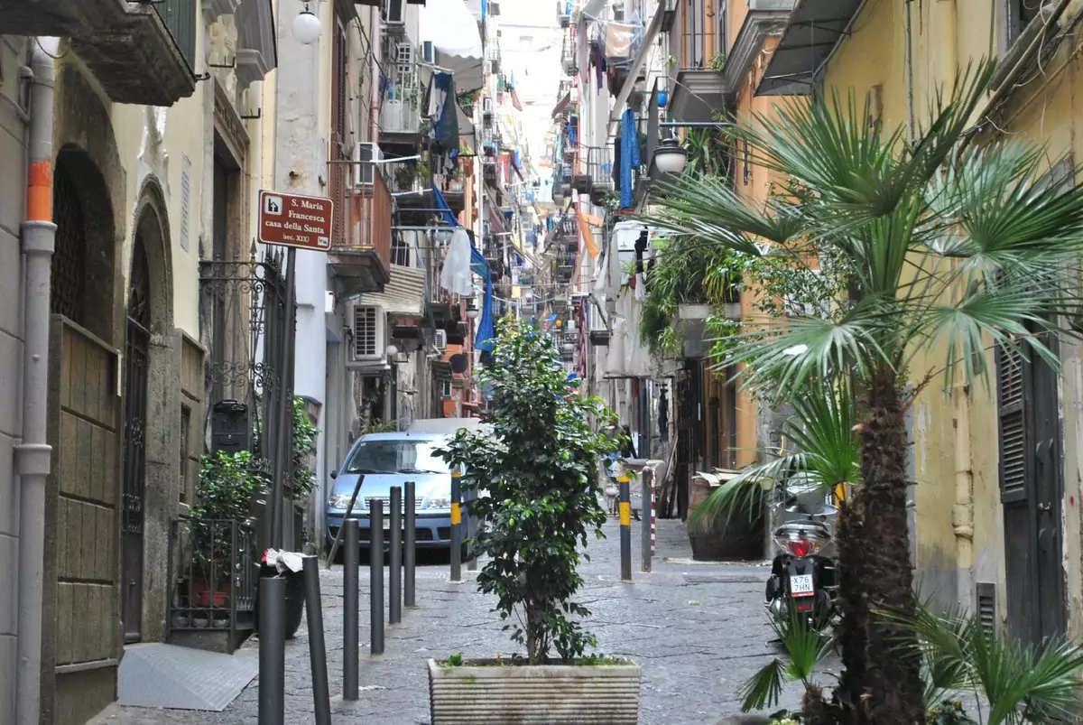 Street scene in the Quartieri Spagnoli district of Naples, Italy, with narrow alleys, colorful buildings, hanging laundry, and scooters lining the cobblestone path, capturing the vibrant local character of the neighborhood.