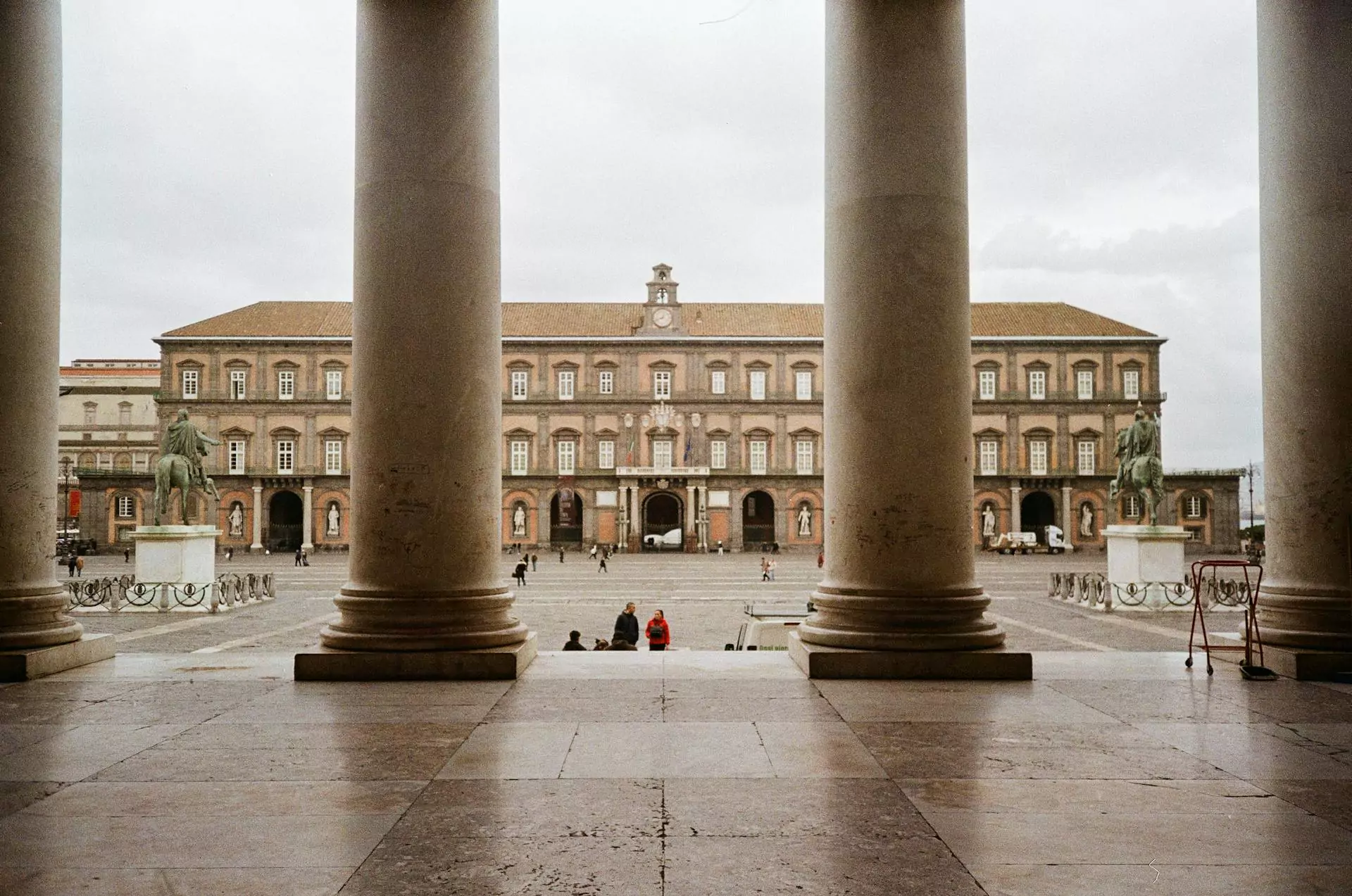 Exterior of the Royal Palace of Naples, Italy, featuring a grand symmetrical façade with arched windows, statues in niches, and a wide courtyard entrance set in the historic Piazza del Plebiscito.