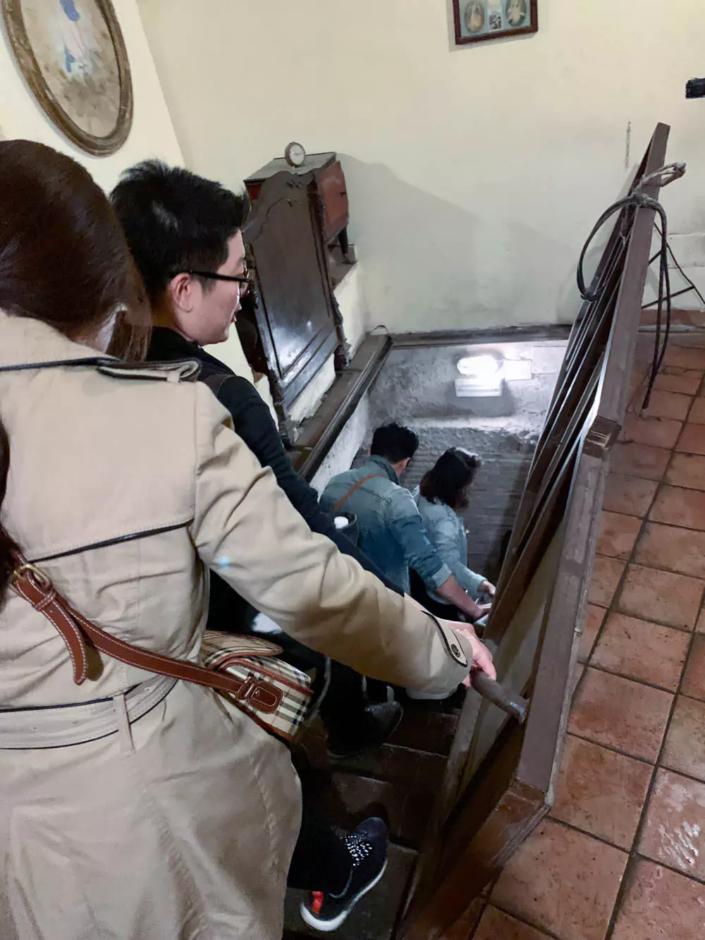 Tourists walking down a narrow staircase from inside a shop to begin the Naples Underground Tour, descending into the ancient tunnels and chambers beneath the city.