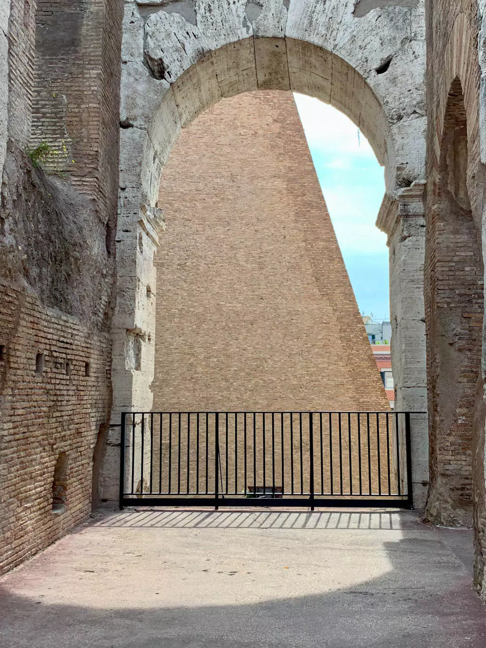 Stone archway inside the Colosseum in Rome, Italy, partially enclosed by a black iron fence, with weathered walls and ancient masonry highlighting the structure’s enduring Roman architecture.