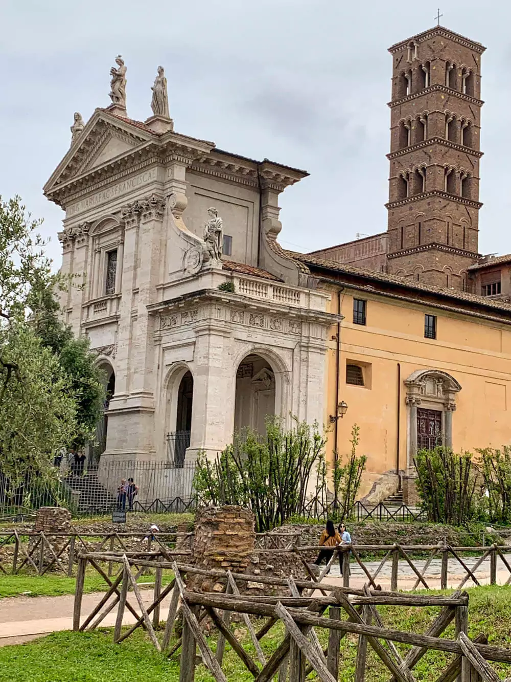 Basilica di Santa Francesca Romana in the Roman Forum, Rome, featuring a Baroque façade with twin bell towers and classical columns, set against the backdrop of ancient ruins and a clear blue sky.