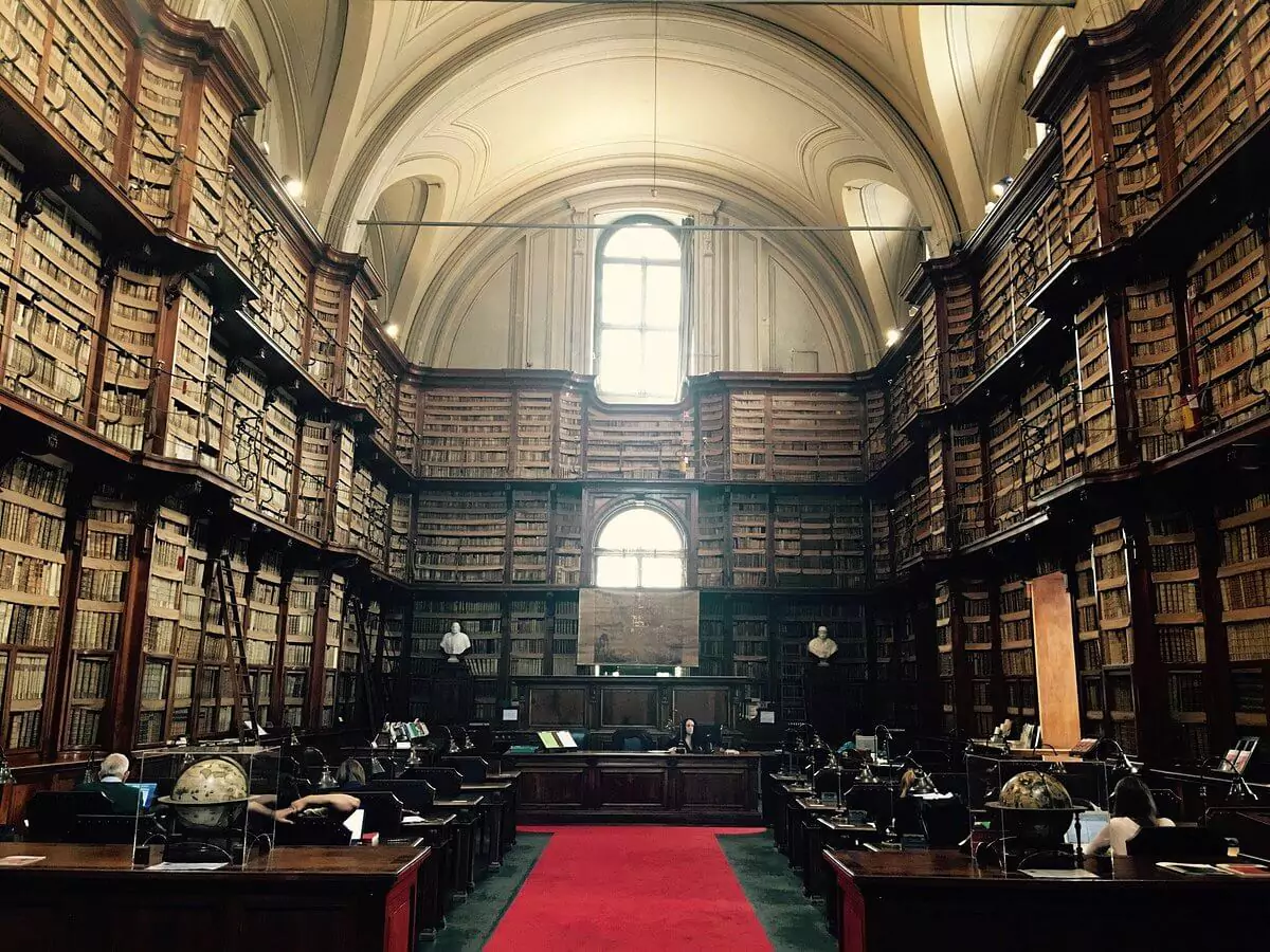 Interior view of the Biblioteca Angelica in Rome, featuring rows of tall wooden bookshelves filled with ancient volumes, arched ceilings, and a serene, scholarly atmosphere.