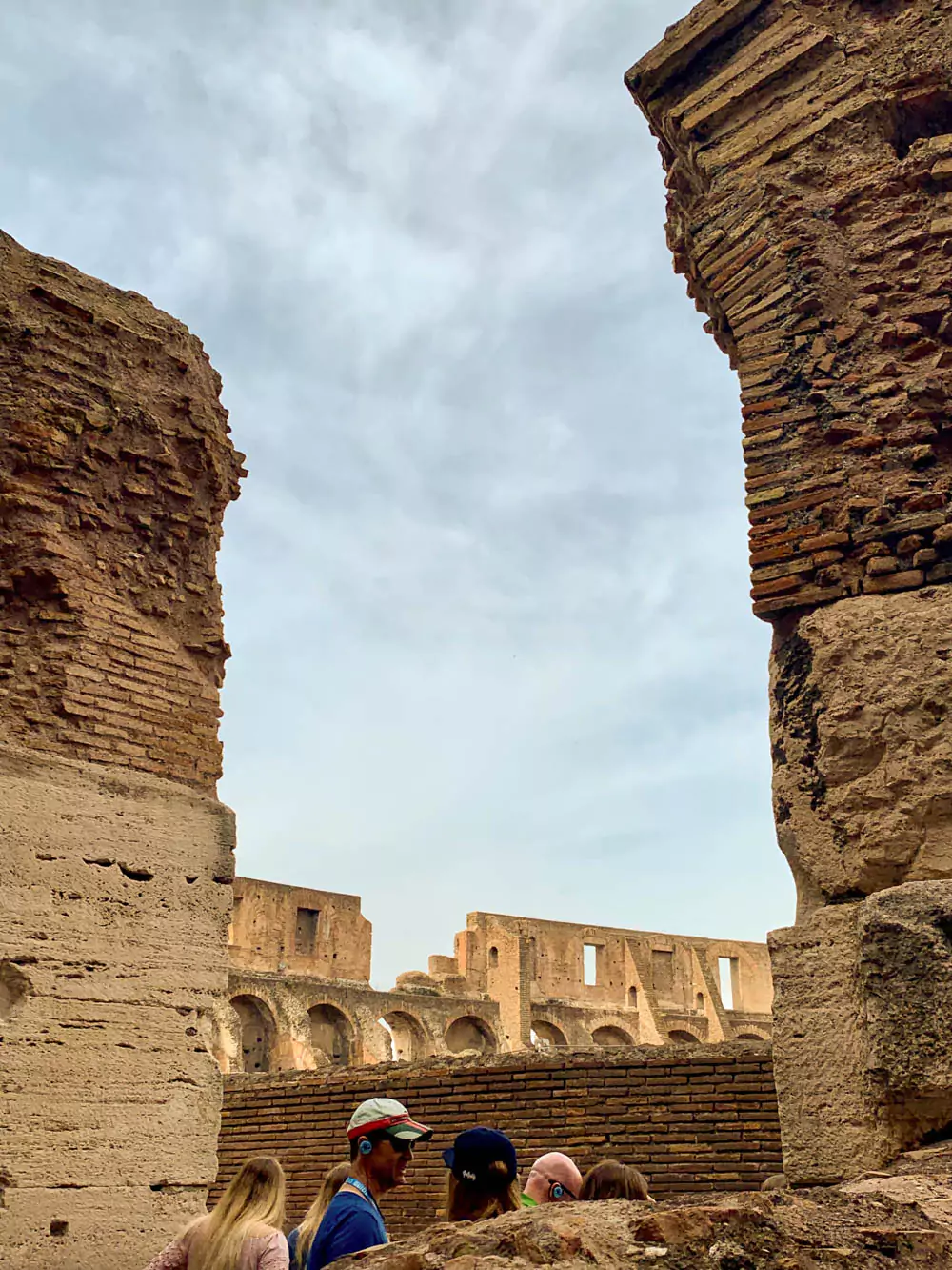Interior view of the Colosseum during a tour, showcasing its impressive architecture, ancient arches, and tiered seating areas under an open sky.