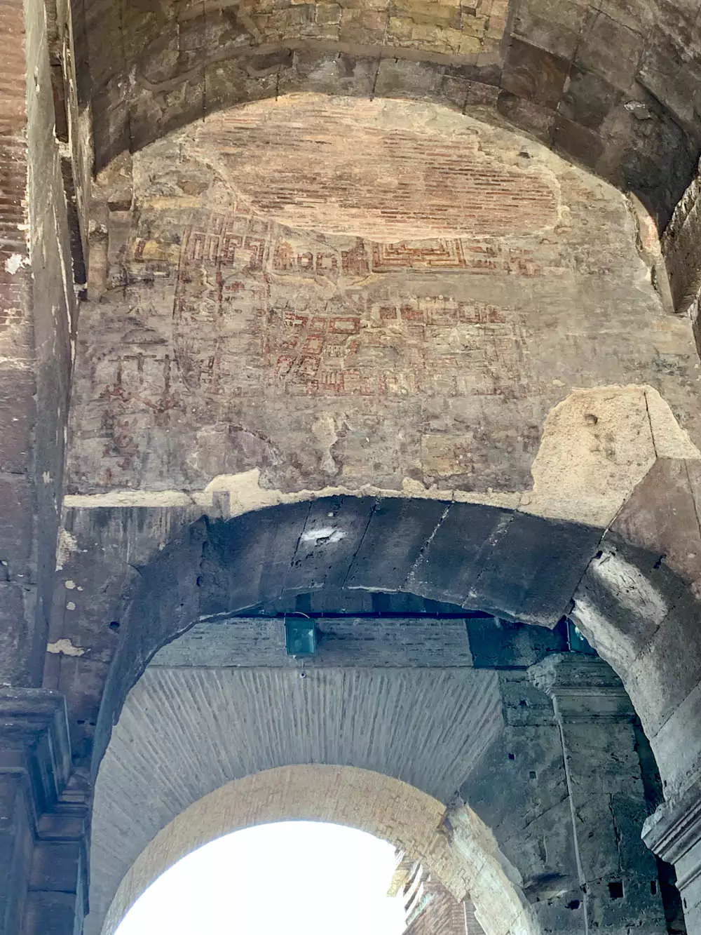 Medieval painting displayed inside the Colosseum in Rome, depicting a stylized view of Jerusalem with the Crucifixion scene near the bottom left, blending religious symbolism with historical context within the ancient amphitheater.