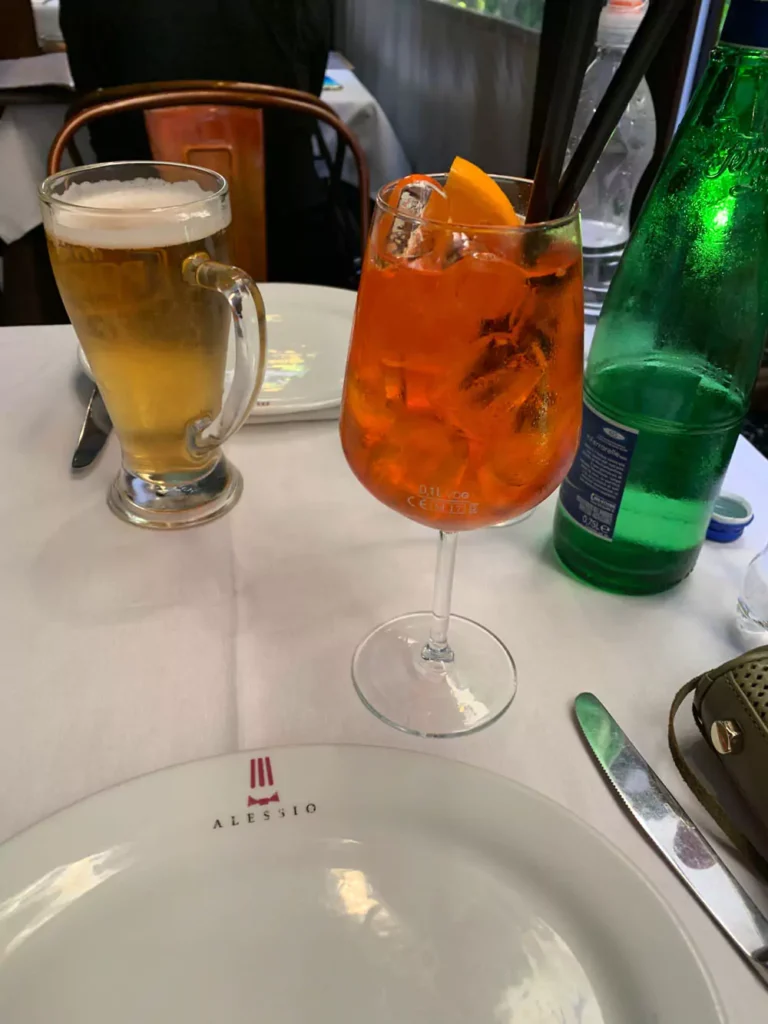 Aperol Spritz served at Ristorante Alessio in Rome, Italy, with the vibrant orange cocktail in a stemmed glass garnished with an orange slice, set on a table with classic Italian decor — a refreshing toast in italy