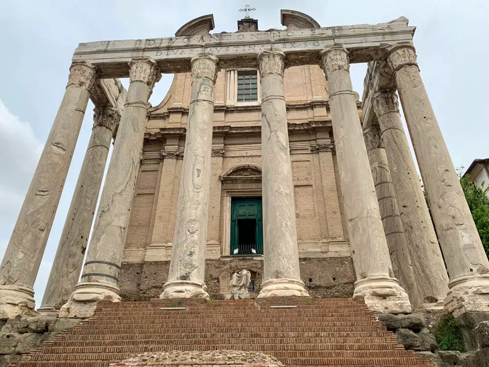 Temple of Antoninus and Faustina in the Roman Forum, Rome, featuring tall Corinthian columns and a well-preserved façade, later converted into a church, blending ancient Roman and medieval architecture.