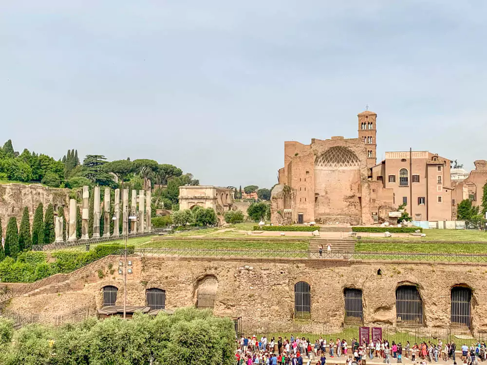 Ruins of the Temple of Venus and Rome in the Roman Forum, featuring towering stone columns and remnants of grand arches, set against the backdrop of ancient pathways and a clear blue sky.