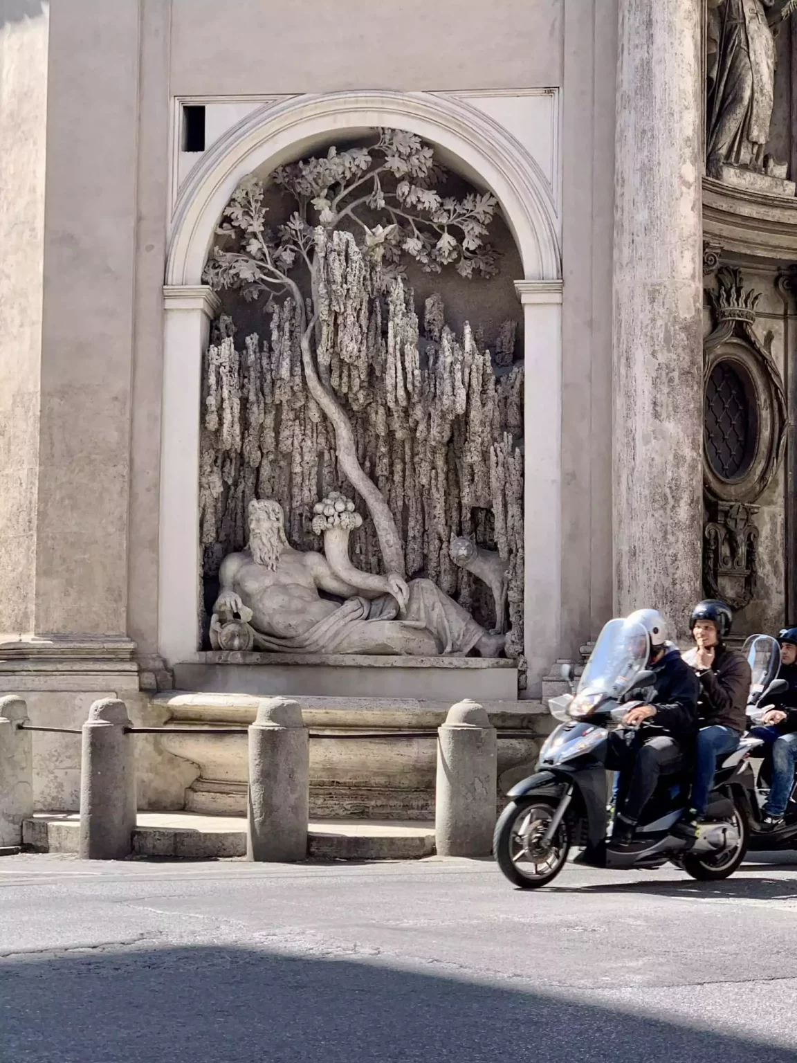 Couple riding a Vespa near San Carlo alle Quattro Fontane in Rome, Italy, with the church’s intricate Baroque facade and curved architecture visible in the background. The classic scooter and historic setting evoke a romantic, quintessentially Italian moment.