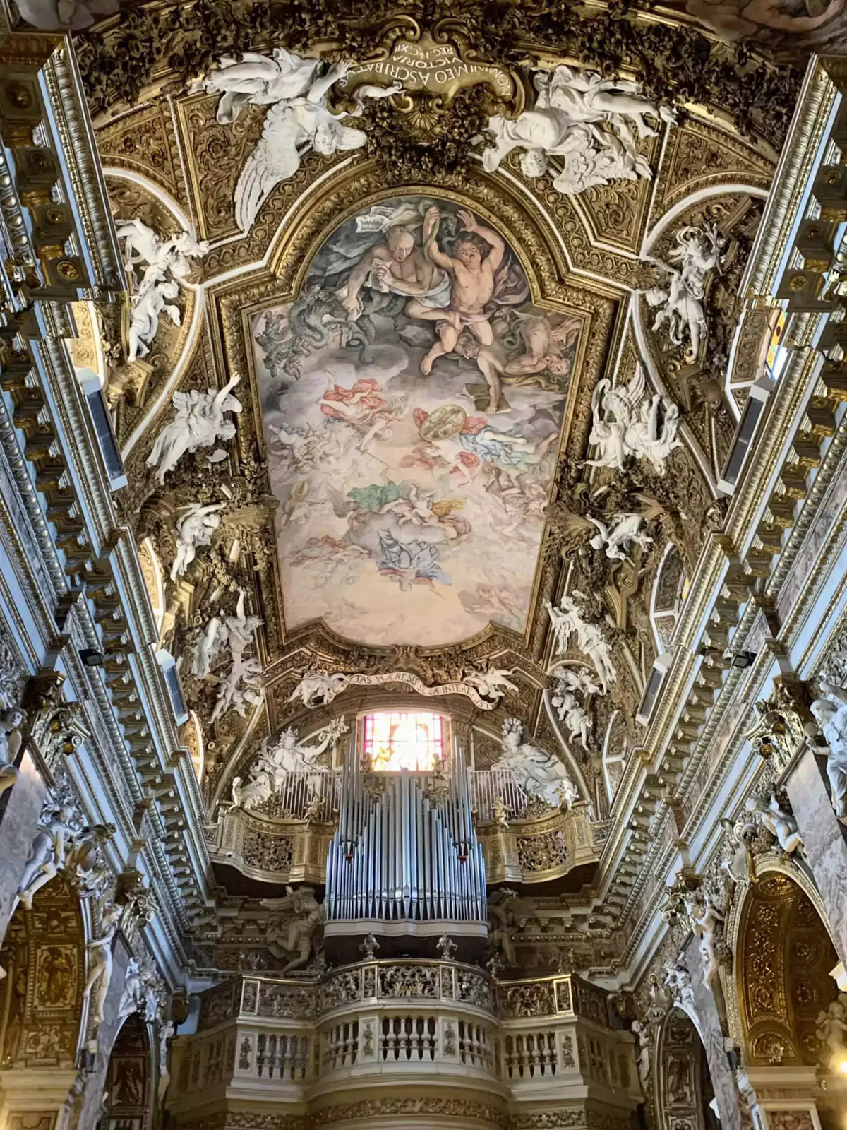 Ornate ceiling of Santa Maria della Vittoria in Rome, Italy, richly decorated with gold accents, frescoes, and intricate Baroque details. The dramatic artwork and architectural flourishes draw the eye upward, reflecting the grandeur of the church’s interior.