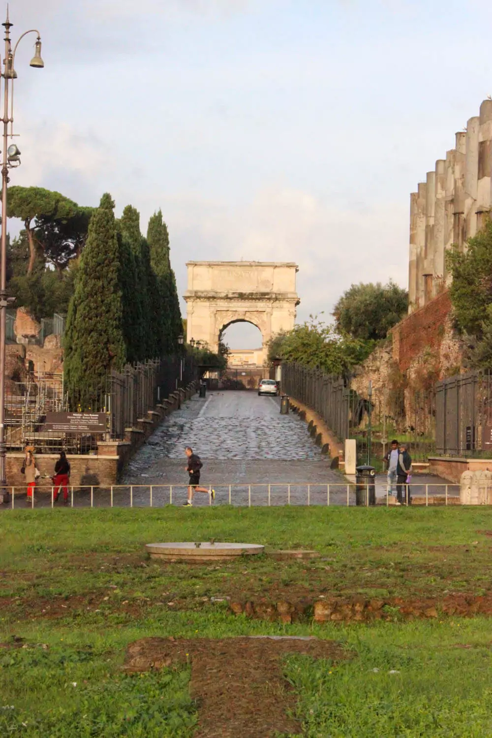 Entrance to the Roman Forum in Rome, Italy, marked by ancient stone pathways and ruins, with arched gateways and informational signs welcoming visitors into the heart of the archaeological site.