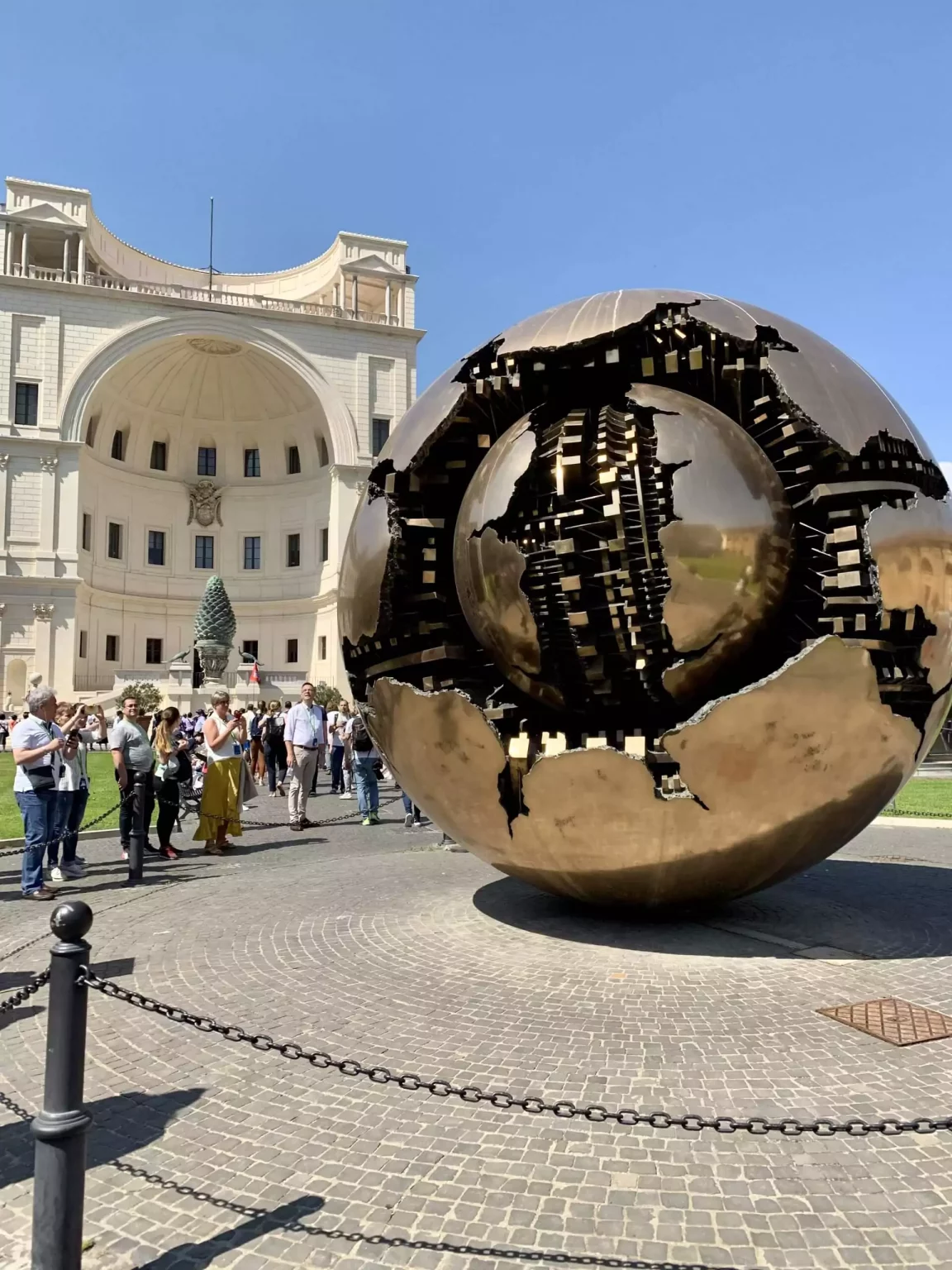 Sphere Within a Sphere by Arnaldo Pomodoro at the Vatican Museums in Rome, featuring a large bronze globe with a fractured, mechanical inner sphere exposed. The modern sculpture contrasts with the historic setting, symbolizing complexity within harmony.