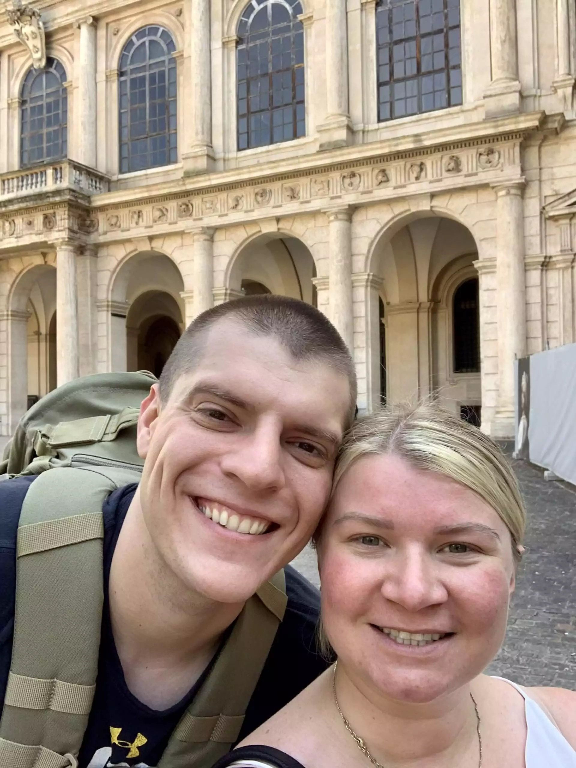 Katie and Zack in Rome, Italy, smiling together with historic Roman architecture and cobblestone streets in the background, capturing a joyful moment during their travels.
