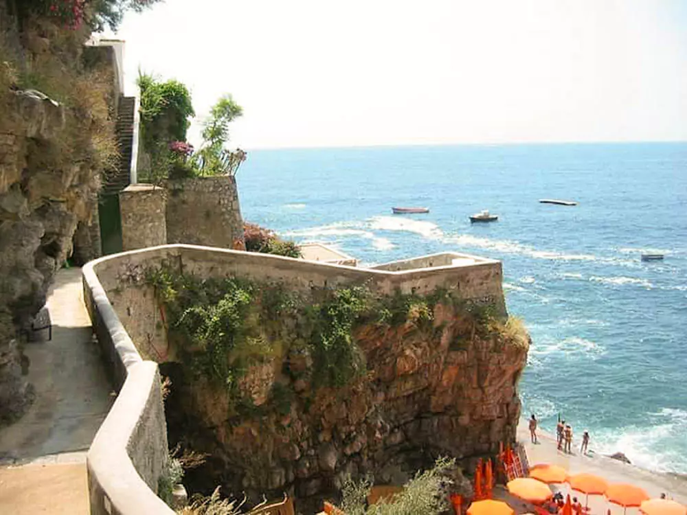 The coastline of Rovigo, Italy, featuring a sandy beach lined with rows of vibrant orange umbrellas, gentle waves lapping the shore, and a relaxed seaside atmosphere