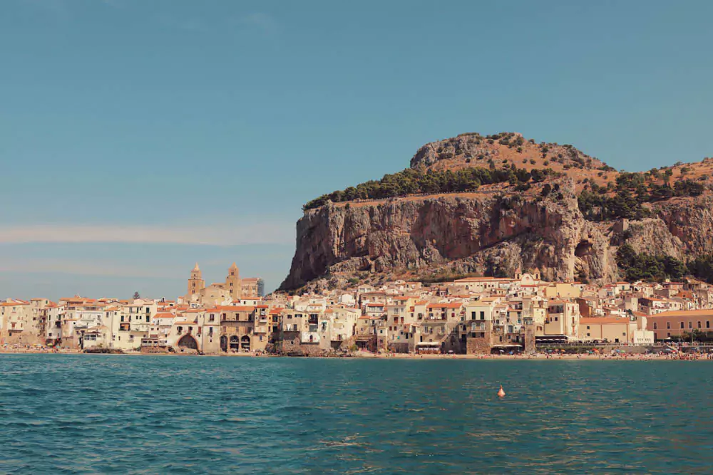 Scenic view of Sicily, Italy, featuring a blend of coastal cliffs, rolling hills, and historic towns, with the blue Mediterranean Sea and Mount Etna often visible in the background.
