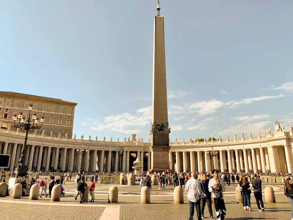 Central obelisk and surrounding colonnade in St. Peter’s Square, Vatican City, with rows of Tuscan columns curving around the plaza and the ancient Egyptian obelisk standing tall beneath a bright sky.