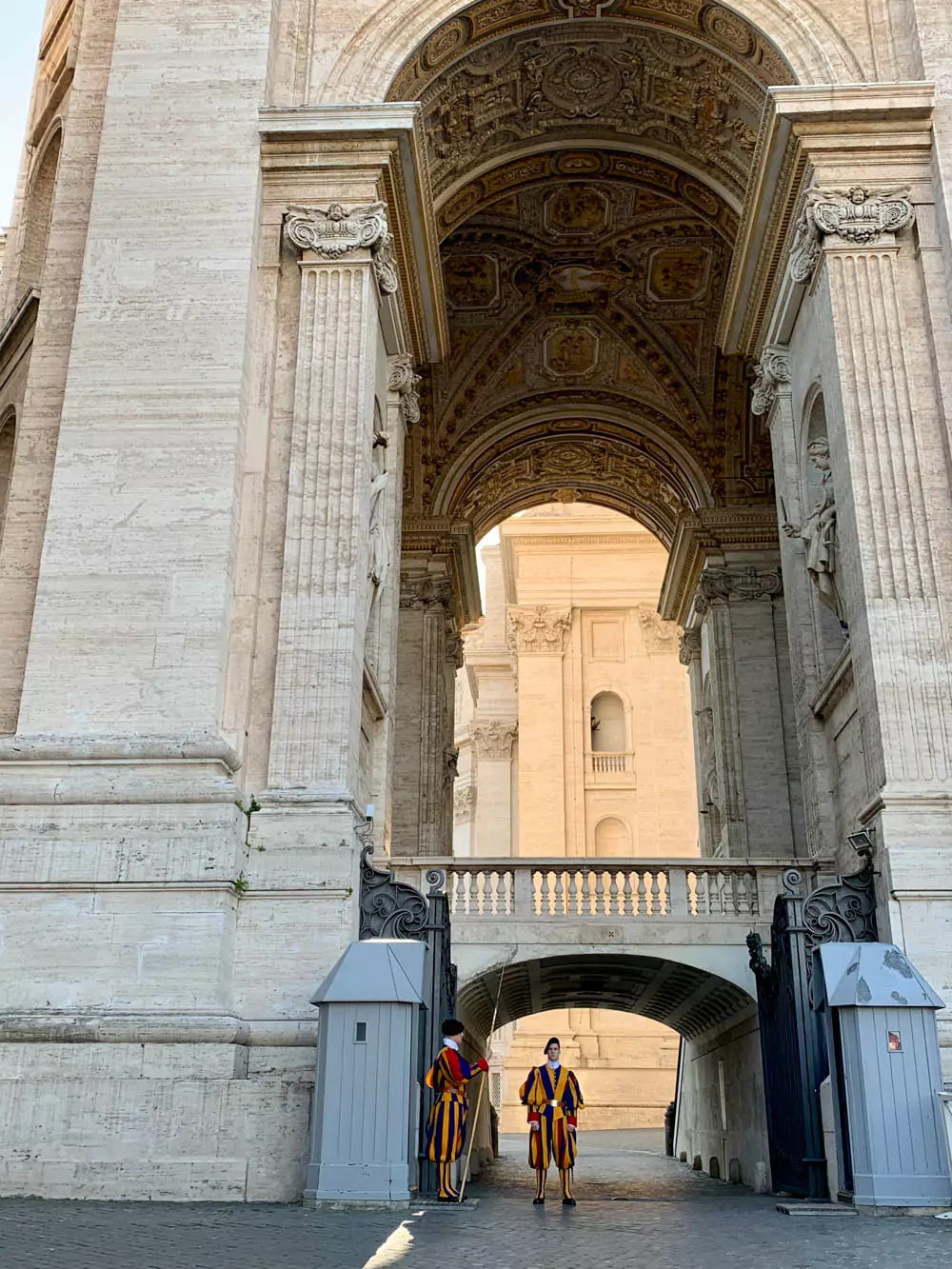 Swiss Guards in traditional blue, red, and yellow Renaissance uniforms standing in St. Peter’s Square, Vatican City, with the grand colonnades and St. Peter’s Basilica in the background.