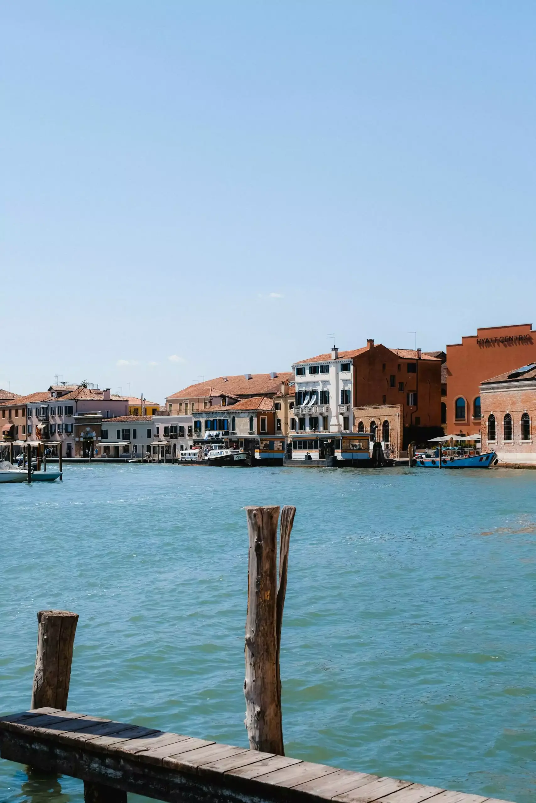 View of Giudecca Island in Venice, Italy, with historic buildings lining the waterfront, boats docked along the edge, and a peaceful atmosphere across the canal from the main city.