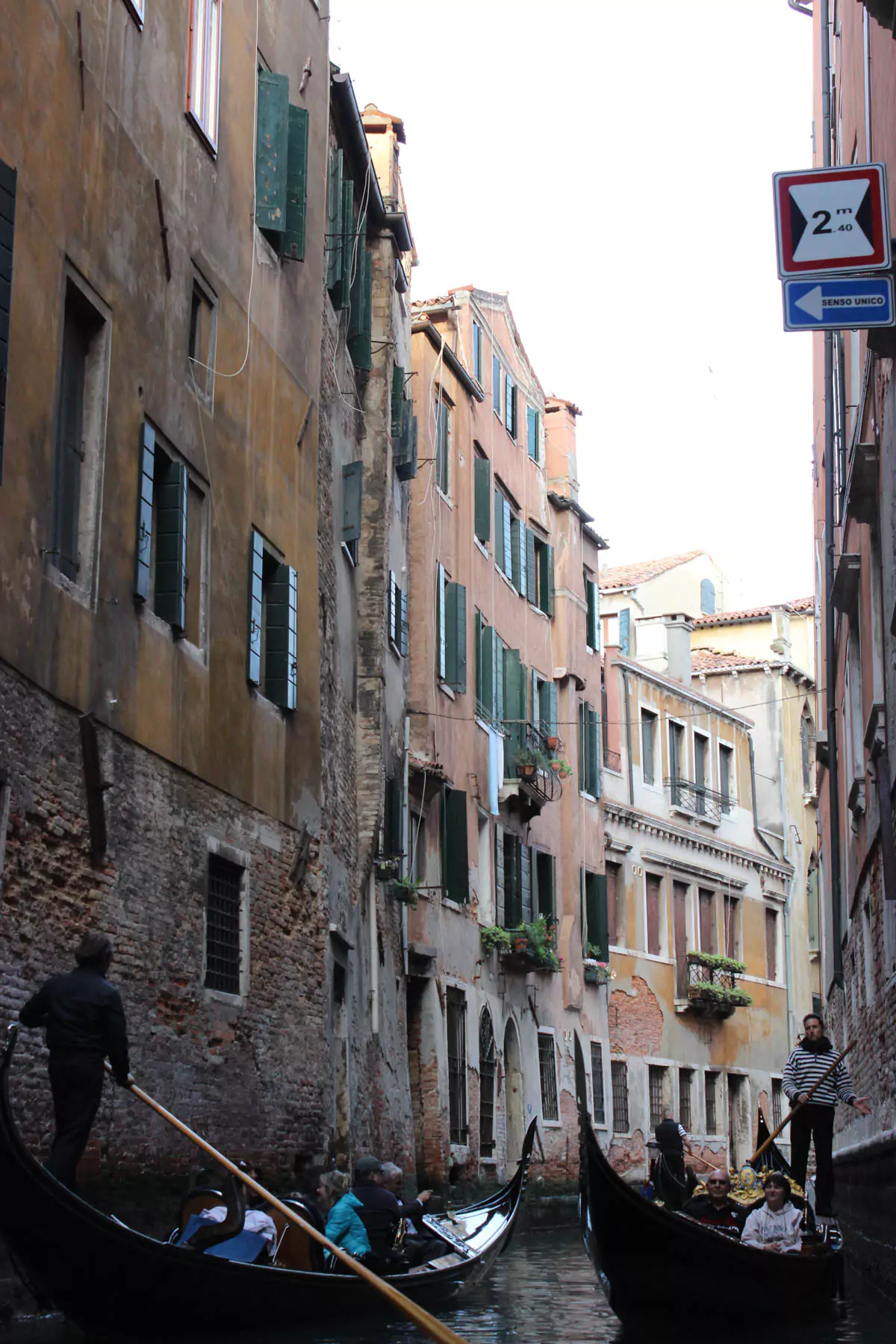 Scenic gondola ride in Venice, Italy, with a gondolier steering through narrow canals lined by historic buildings. The calm water reflects the architecture, creating a romantic and iconic Venetian experience.