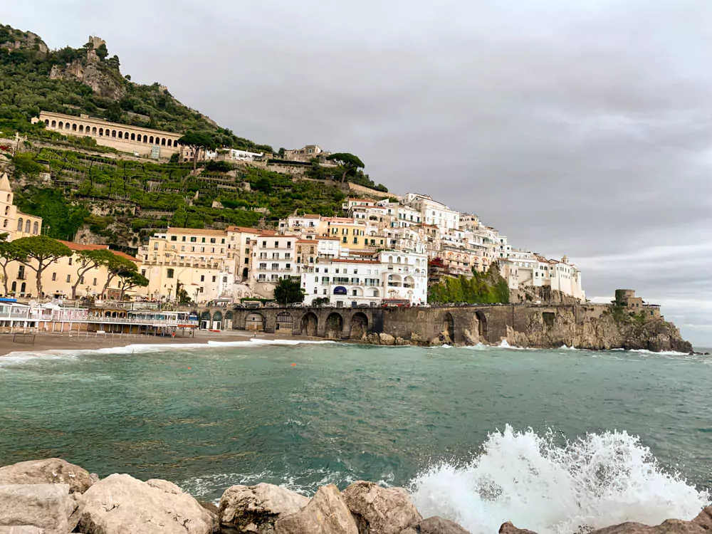 View of colorful buildings stacked along the steep coastline of Amalfi town in the Amalfi Coast, Italy, with terraced architecture overlooking the turquoise Mediterranean Sea.