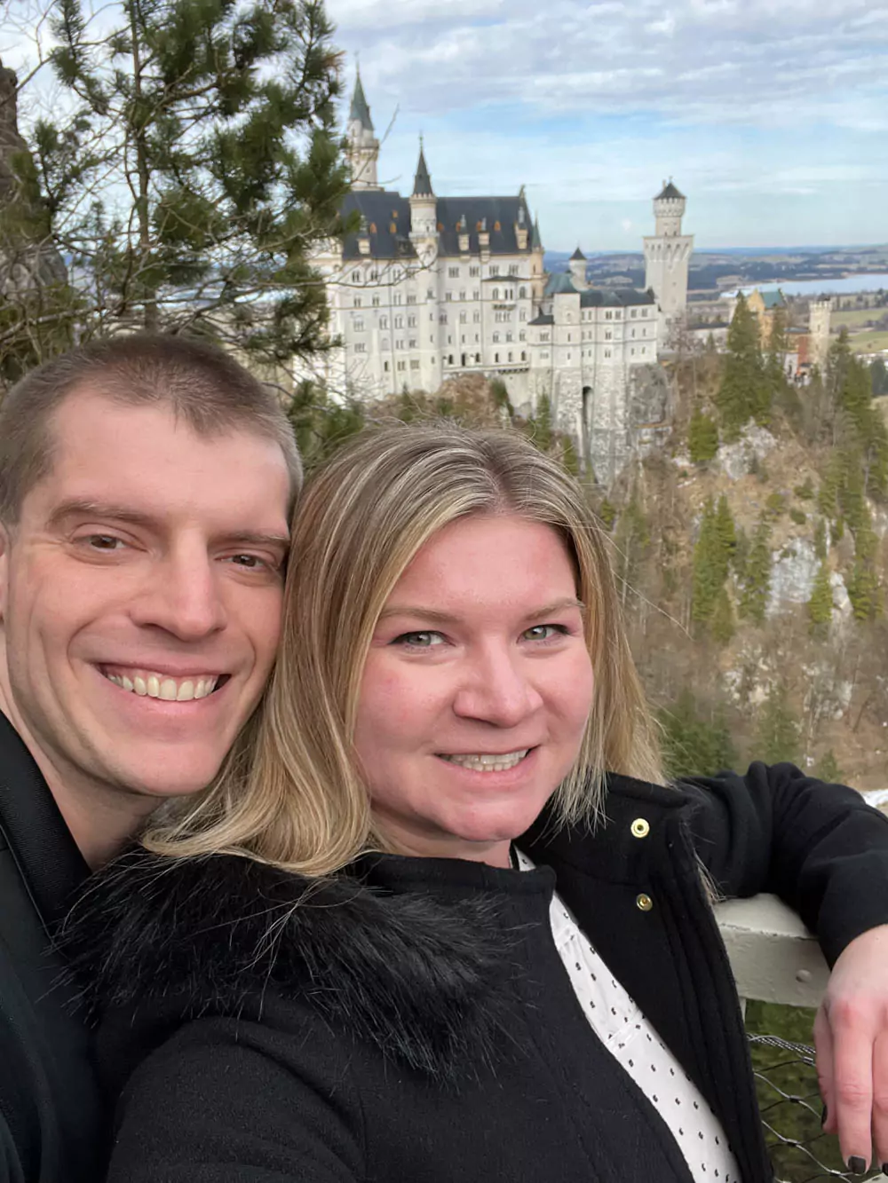Katie and Zack standing on Marienbrücke, the scenic footbridge overlooking Neuschwanstein Castle in Bavaria, Germany, with the castle’s iconic towers rising behind them and alpine cliffs all around.