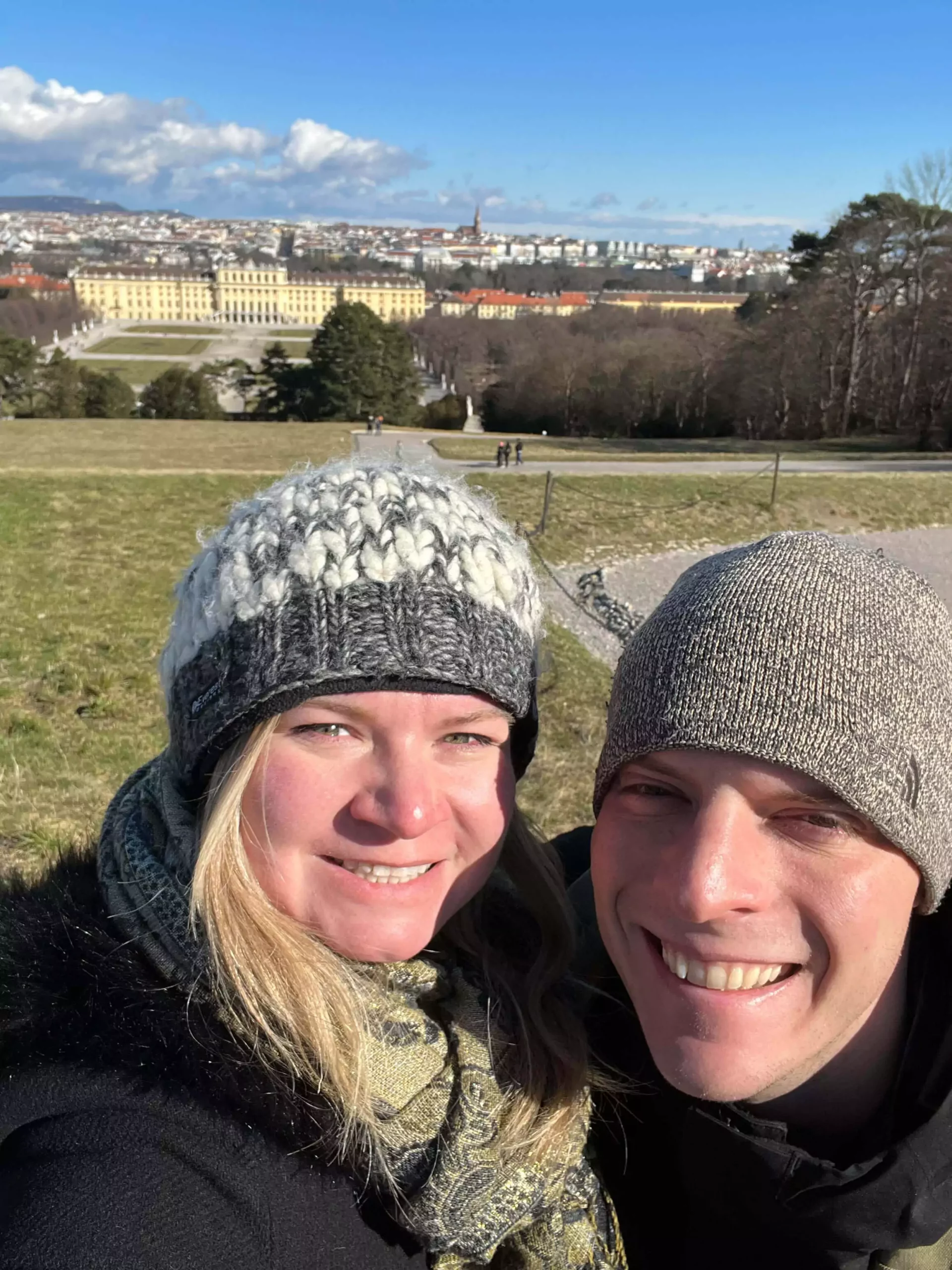 Katie and Zack standing on top of Schönbrunn Hill in Vienna, Austria, with panoramic views of the Baroque Schönbrunn Palace and its formal gardens stretching out below.
