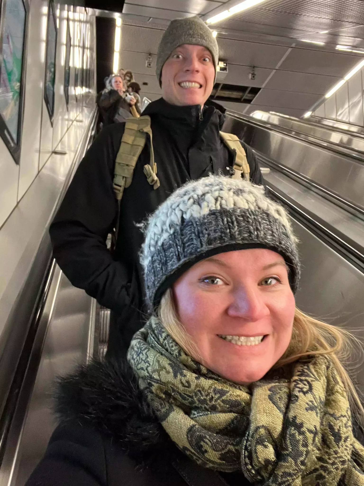 Katie and Zack take a fun selfie on the escalator heading down to the subway in Vienna, Austria. The tunnel walls and lighting create a dynamic backdrop as they capture a candid moment in transit.