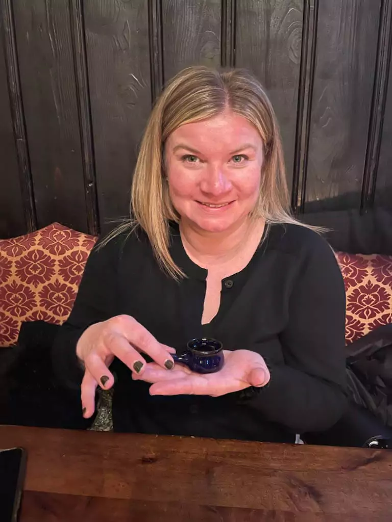 Katie holds a tiny jar of schnapps and smiles at Im Keller, a cozy, rustic bar in Nuremberg, Germany. The dim lighting and stone walls hint at the venue’s cellar-like charm, giving the moment a warm, intimate vibe.