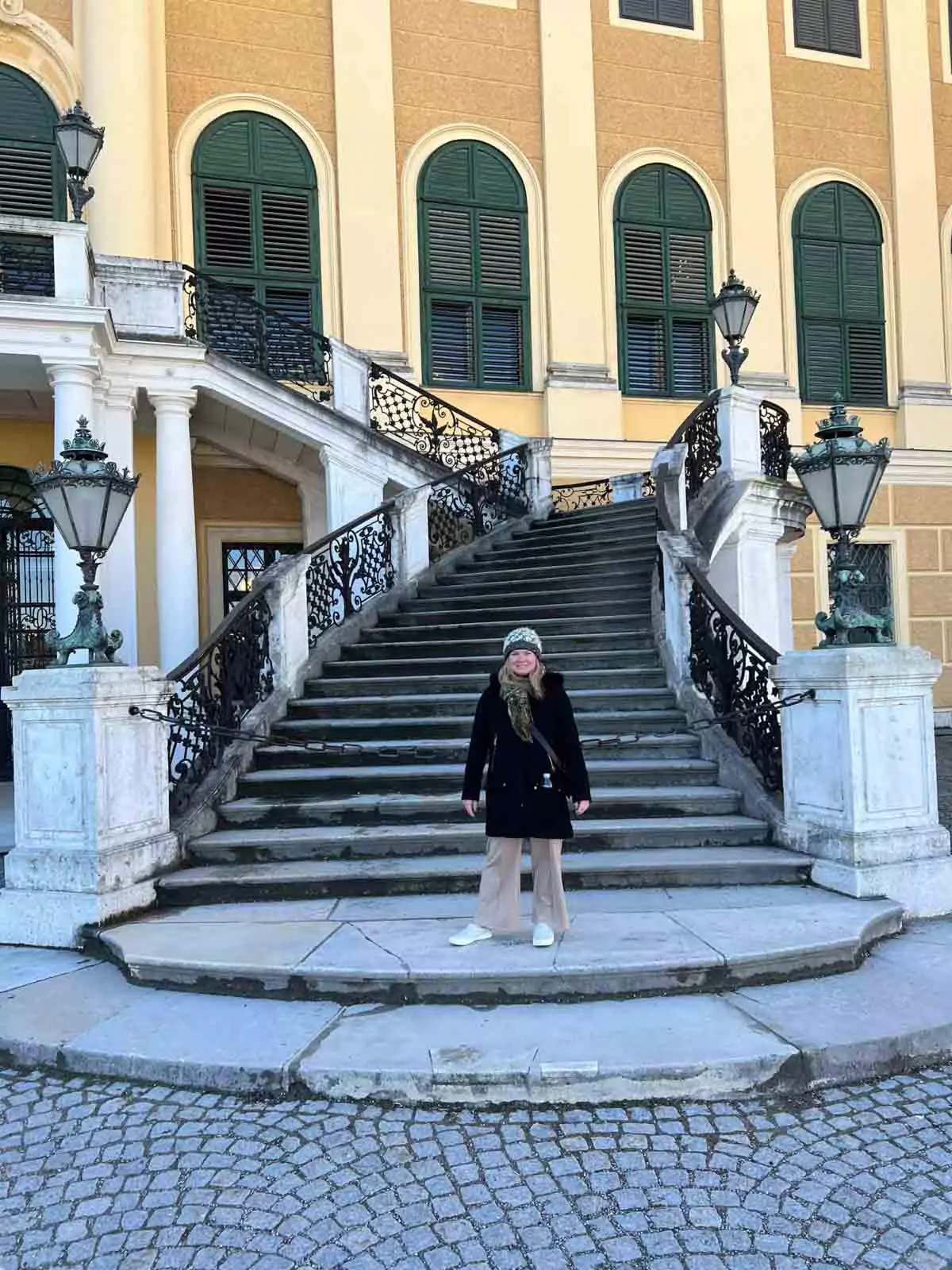 Katie standing in front of a grand stone staircase at Schloss Schönbrunn in Vienna, Austria, with the palace’s elegant baroque architecture rising behind her.