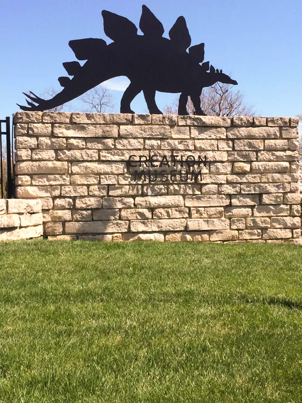 The entrance to the Creation Museum in Kentucky, featuring large columns and a sign with the museum’s name. The building is set against a clear sky with surrounding landscaped greenery.