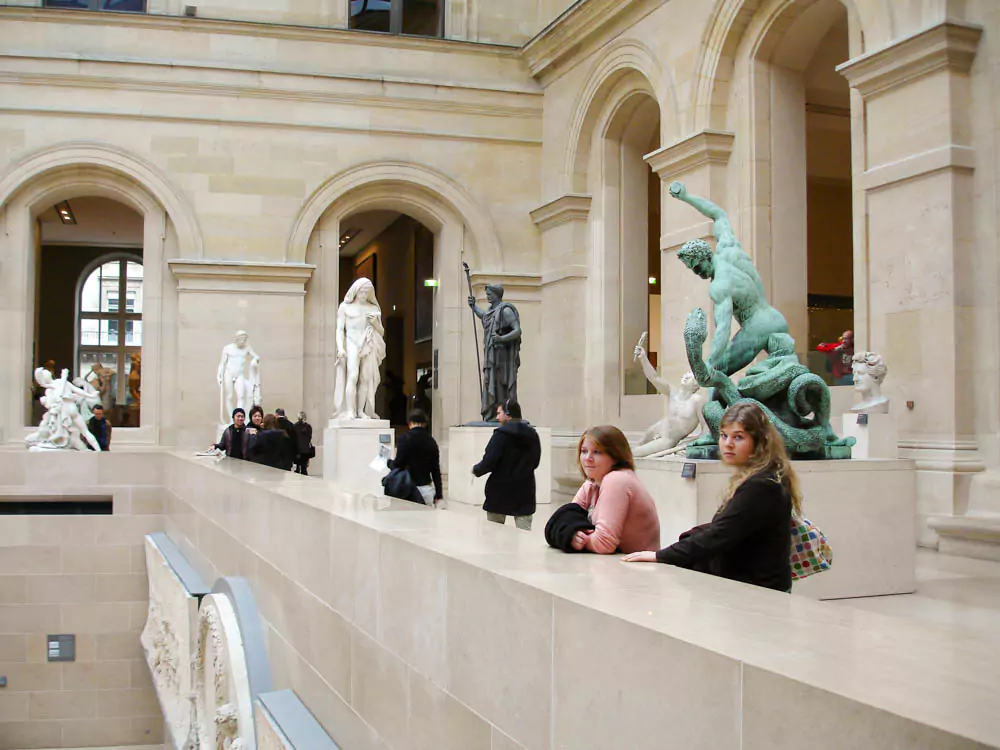 Katie and her sister Mary in front of the Louvre Museum in Paris, January 2006, bundled in winter coats and smiling.