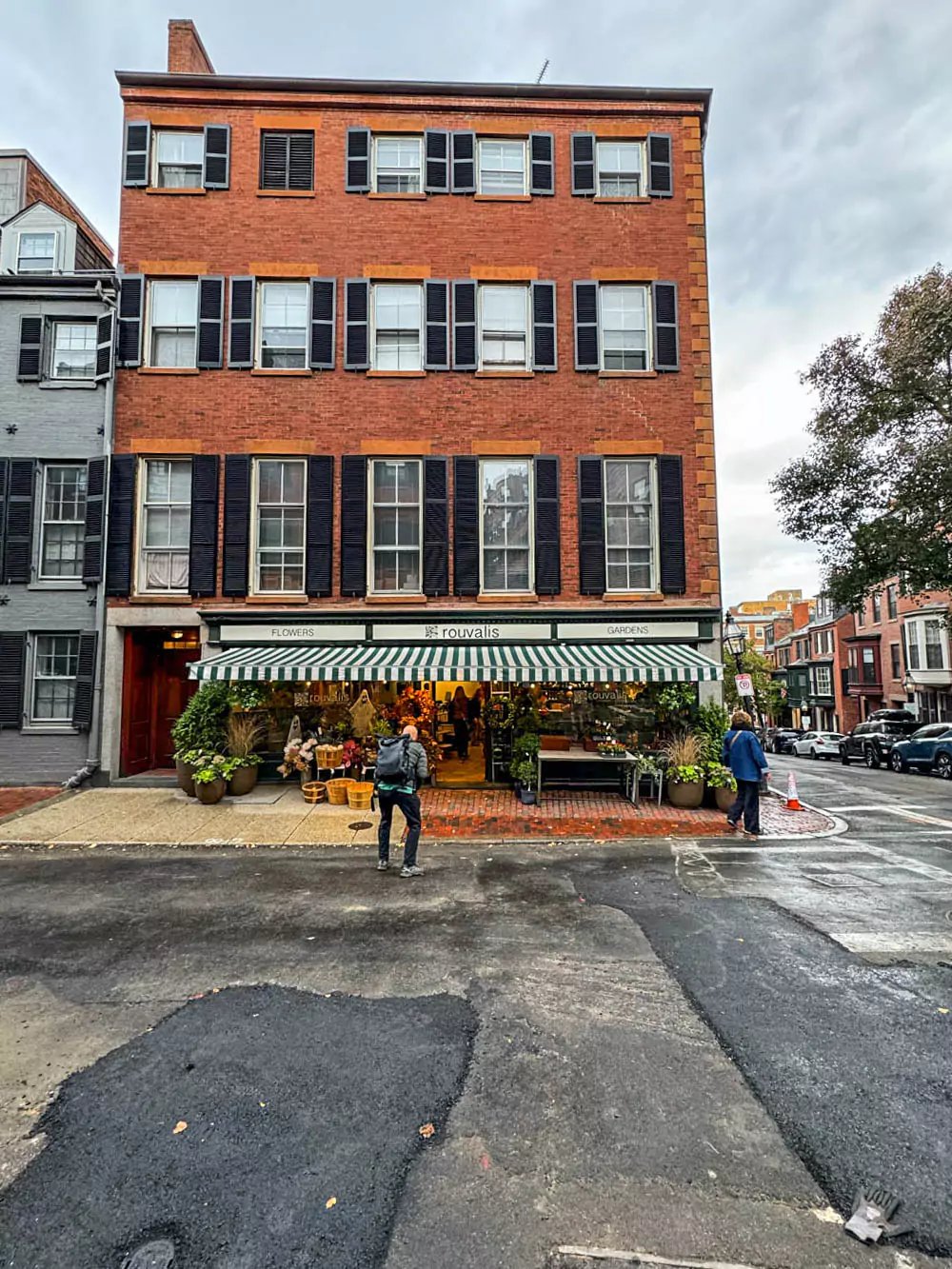Exterior of Rouvalis Flowers in Boston’s Beacon Hill neighborhood, featuring a charming brick facade adorned with lush greenery and vibrant floral displays. The classic storefront blends beautifully with the historic, tree-lined street.