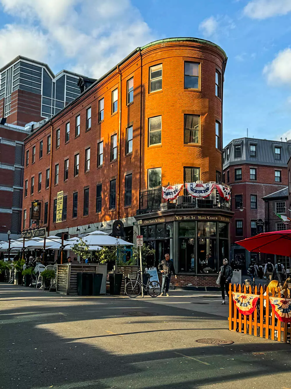 Exterior of the Bell in Hand Tavern in Boston, Massachusetts, featuring a classic brick facade with the tavern’s historic signage and American flags above the entrance. As one of the oldest bars in the U.S., it reflects the city’s rich colonial past.