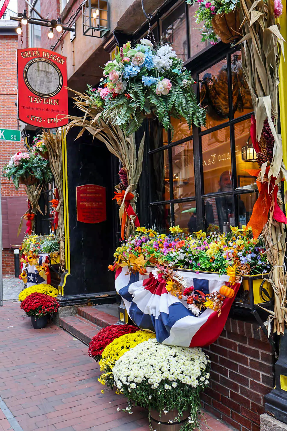 Fall decorations at the entrance of the Green Dragon Tavern in Boston, featuring pumpkins, gourds, and autumn leaves surrounding the historic brick facade. The cozy display adds festive charm to the legendary colonial-era pub.