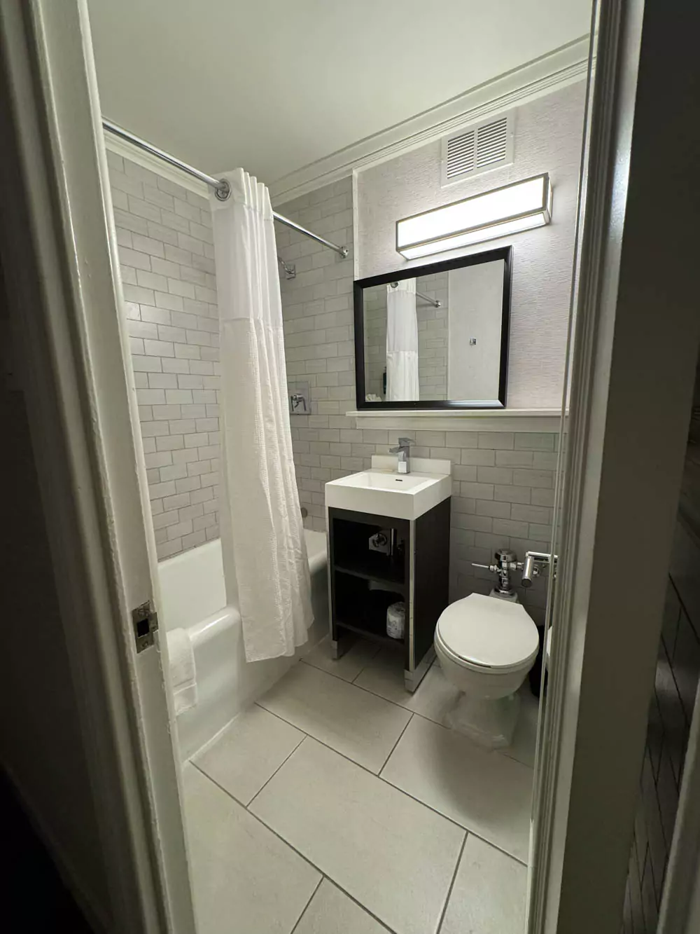 Modern bathroom at the Hilton Boston, featuring a sleek vanity with a large mirror, bright lighting, glass-enclosed shower, and contemporary fixtures.