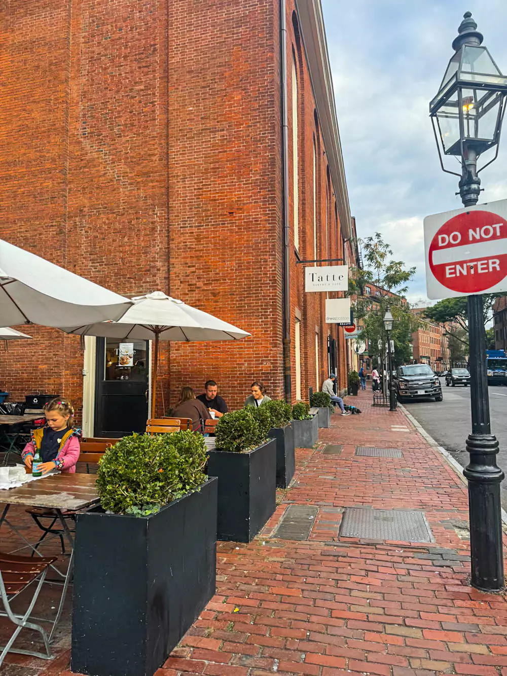 Exterior of Tatte Bakery in Boston’s Beacon Hill, featuring a charming storefront with large windows, a black awning, and potted plants. The inviting café blends modern elegance with the historic charm of the neighborhood.