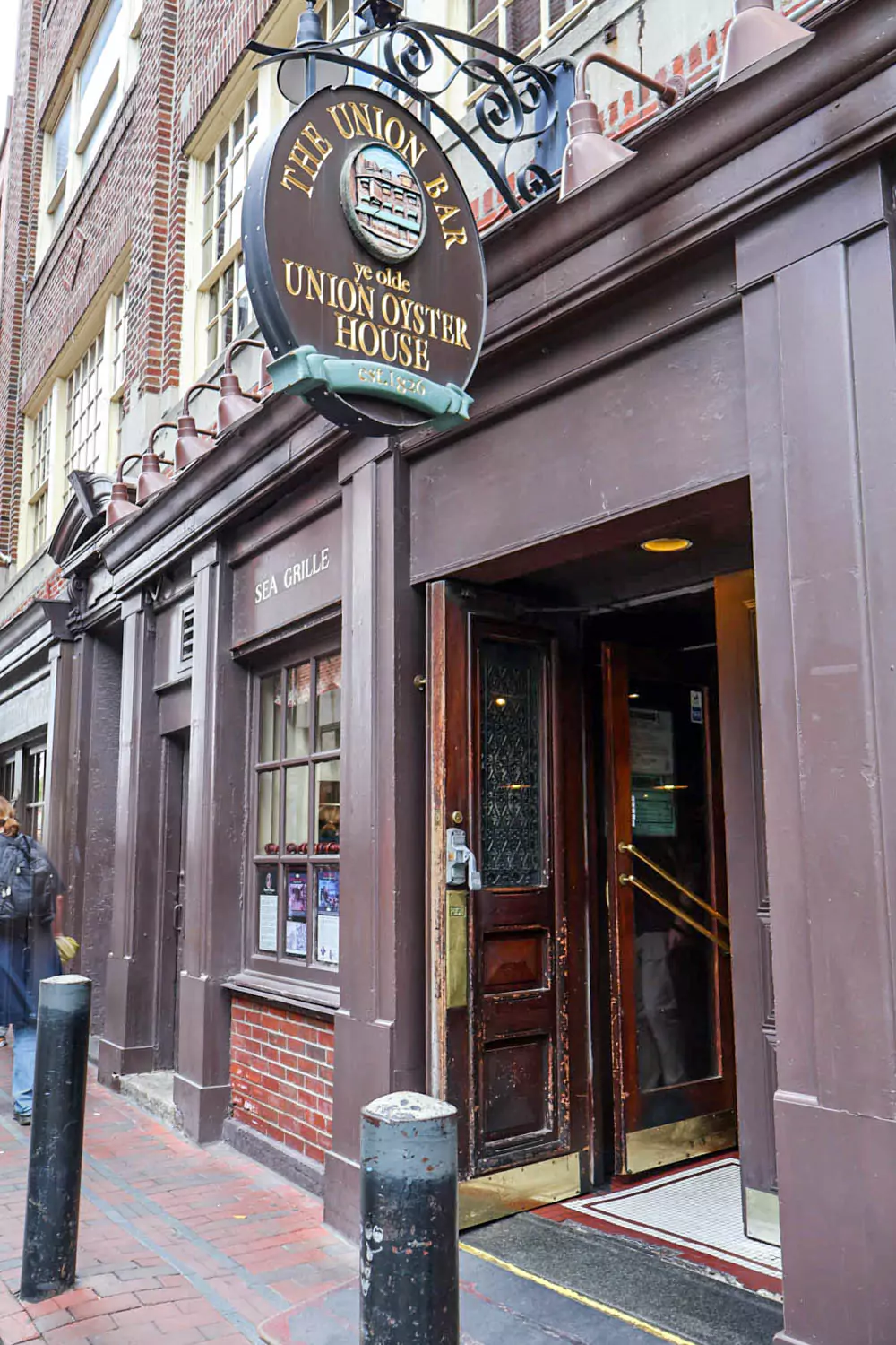 Historic red-brick exterior of Ye Olde Union Oyster House in Boston, with its green-trimmed windows and a classic sign hanging above the entrance. The colonial-style building is one of America’s oldest restaurants, bustling with visitors on the sidewalk outside.