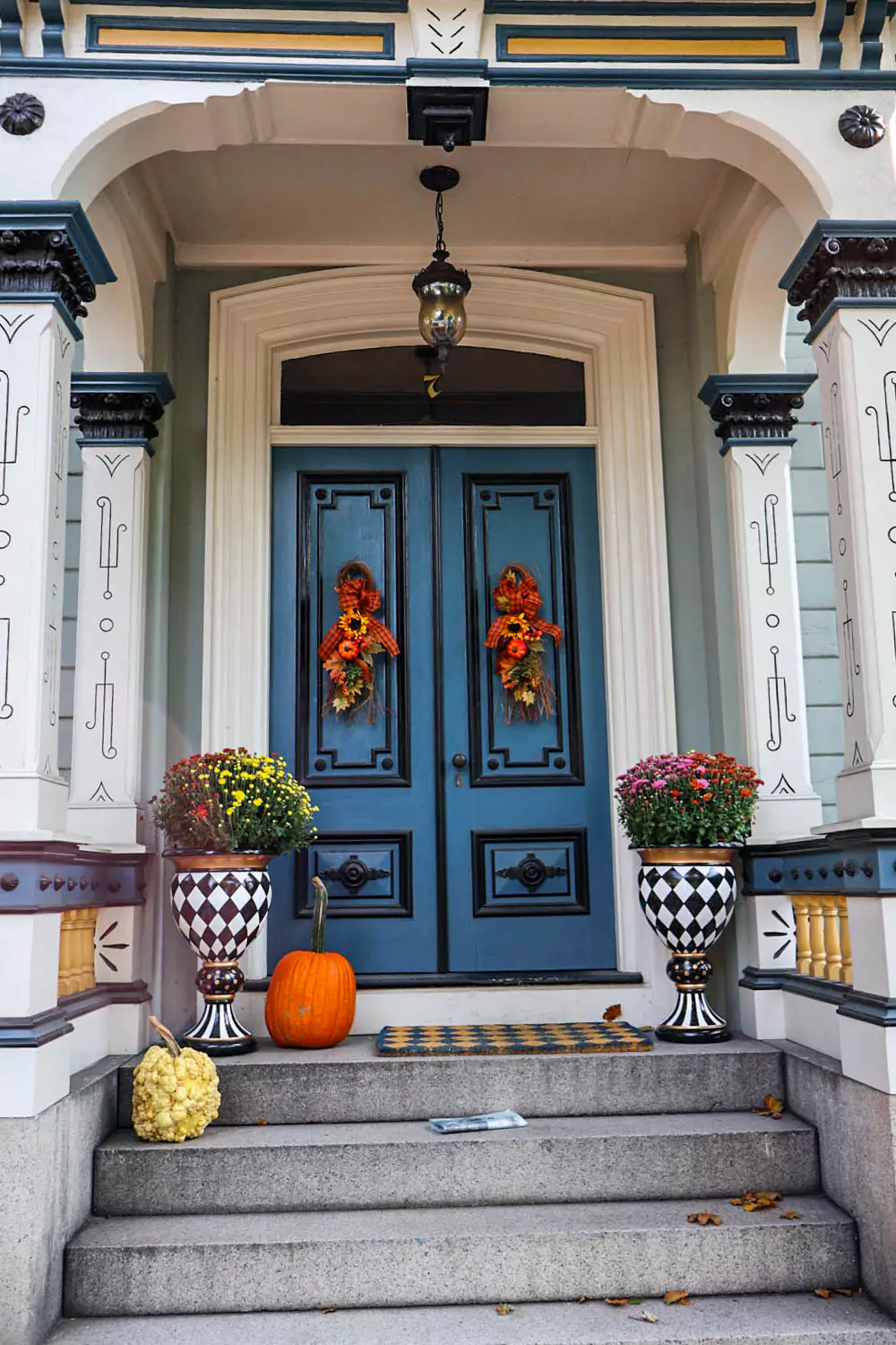 Festive fall front porch in Salem, Massachusetts, featuring a blue door, brick stairs, and seasonal decor including pumpkins, mums, and a rustic wreath. The cozy display welcomes autumn with charm and historic New England character.