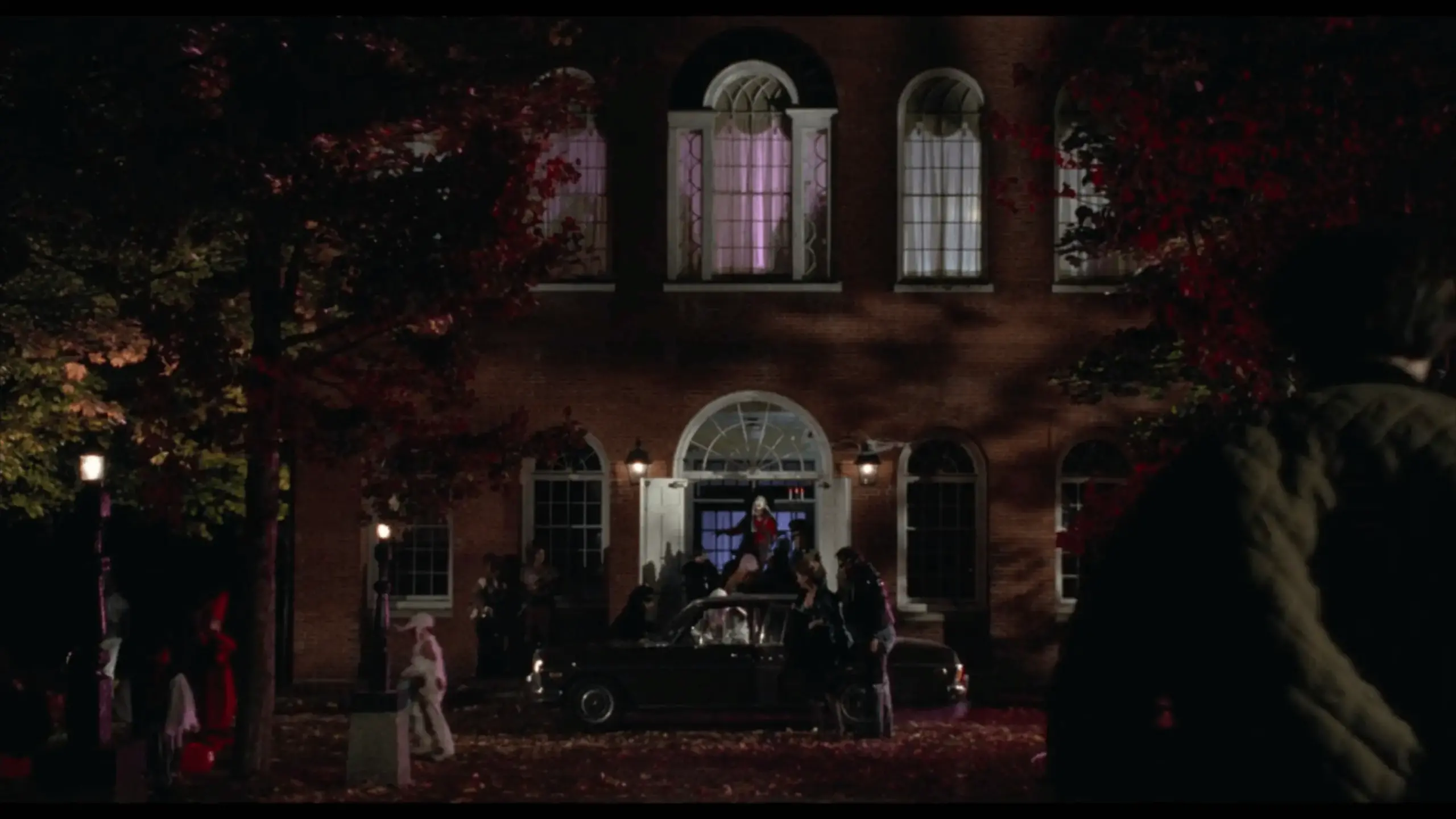 A nighttime screenshot from Hocus Pocus showing Salem Old Town Hall illuminated with warm lights, its red-brick facade and white cupola glowing against the dark sky. The scene captures the building’s spooky, atmospheric role in the film’s setting.