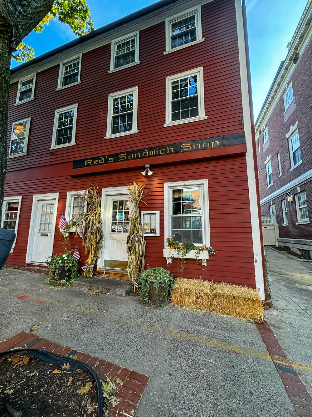 The welcoming entrance of Red’s Sandwich Shop in Boston, featuring a bright red awning with the shop’s name and a glass door inviting customers inside. The storefront is set on a bustling city sidewalk with a classic urban vibe.